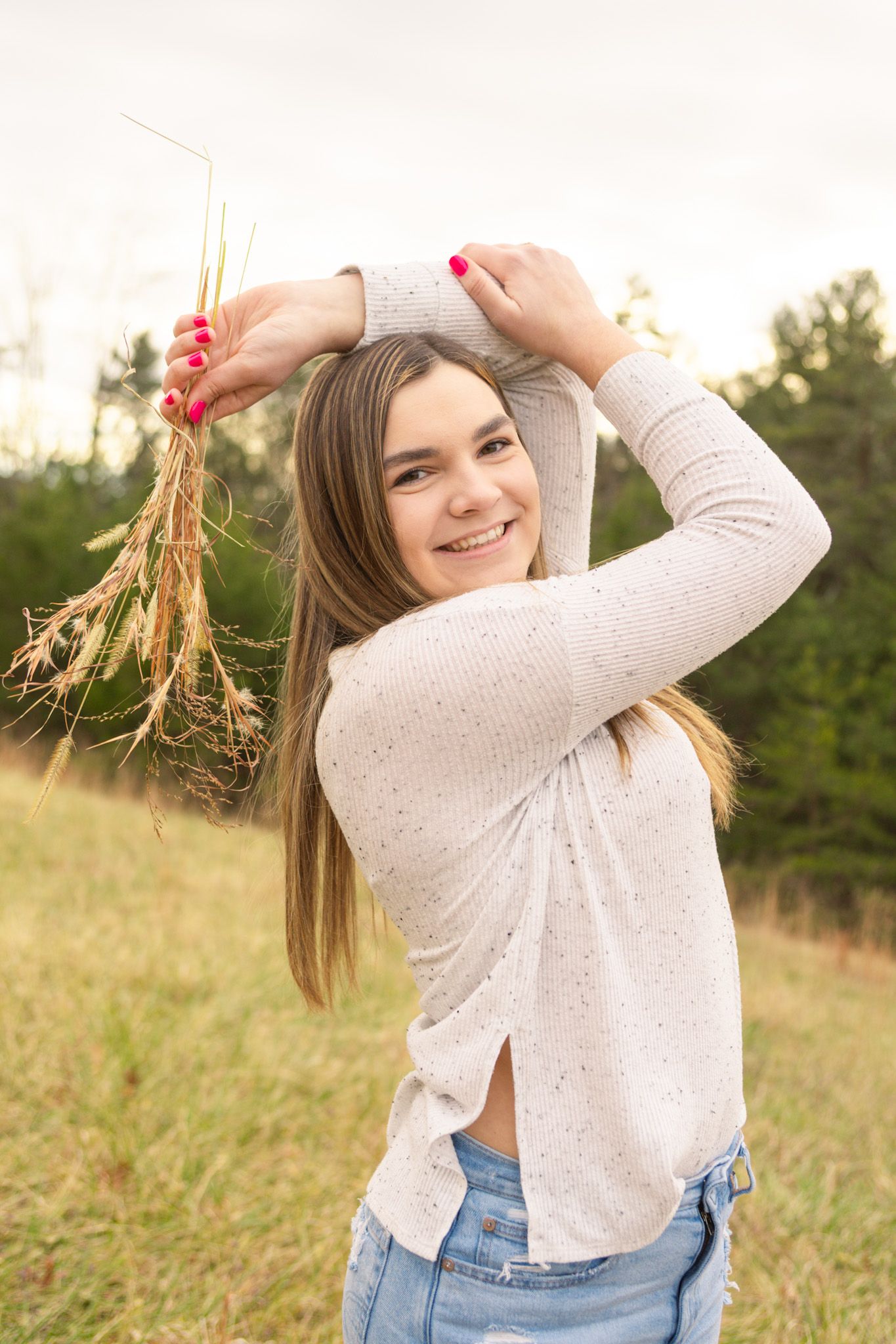 Smiling teenage girl holding wildflowers above her head in a sunlit autumn field.
