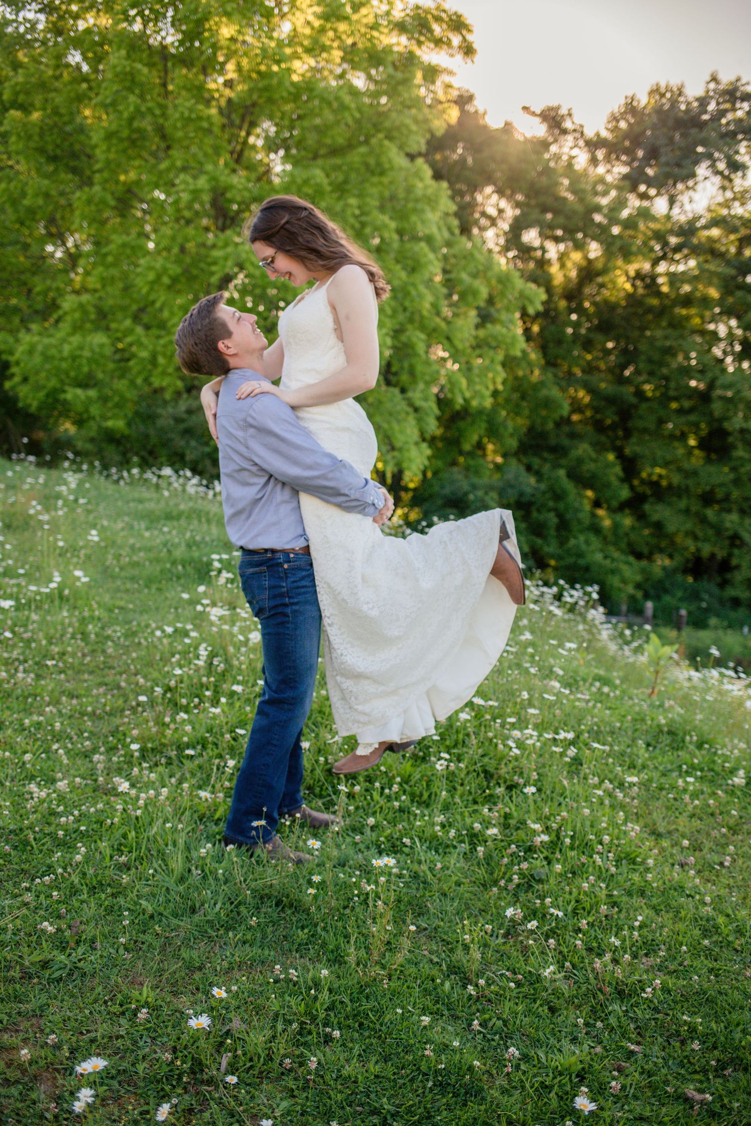 Groom lifting bride in white dress in a wildflower meadow at golden hour sunset.