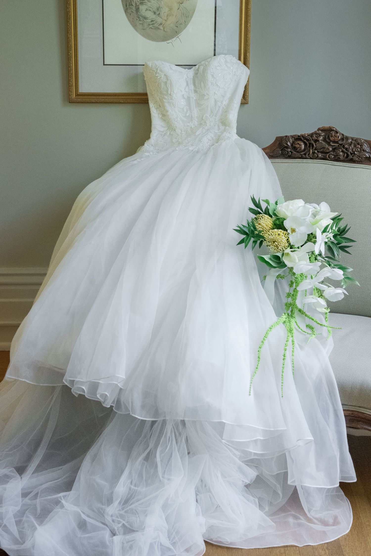 White strapless ball gown wedding dress with lace bodice displayed on chair with white floral bouquet.