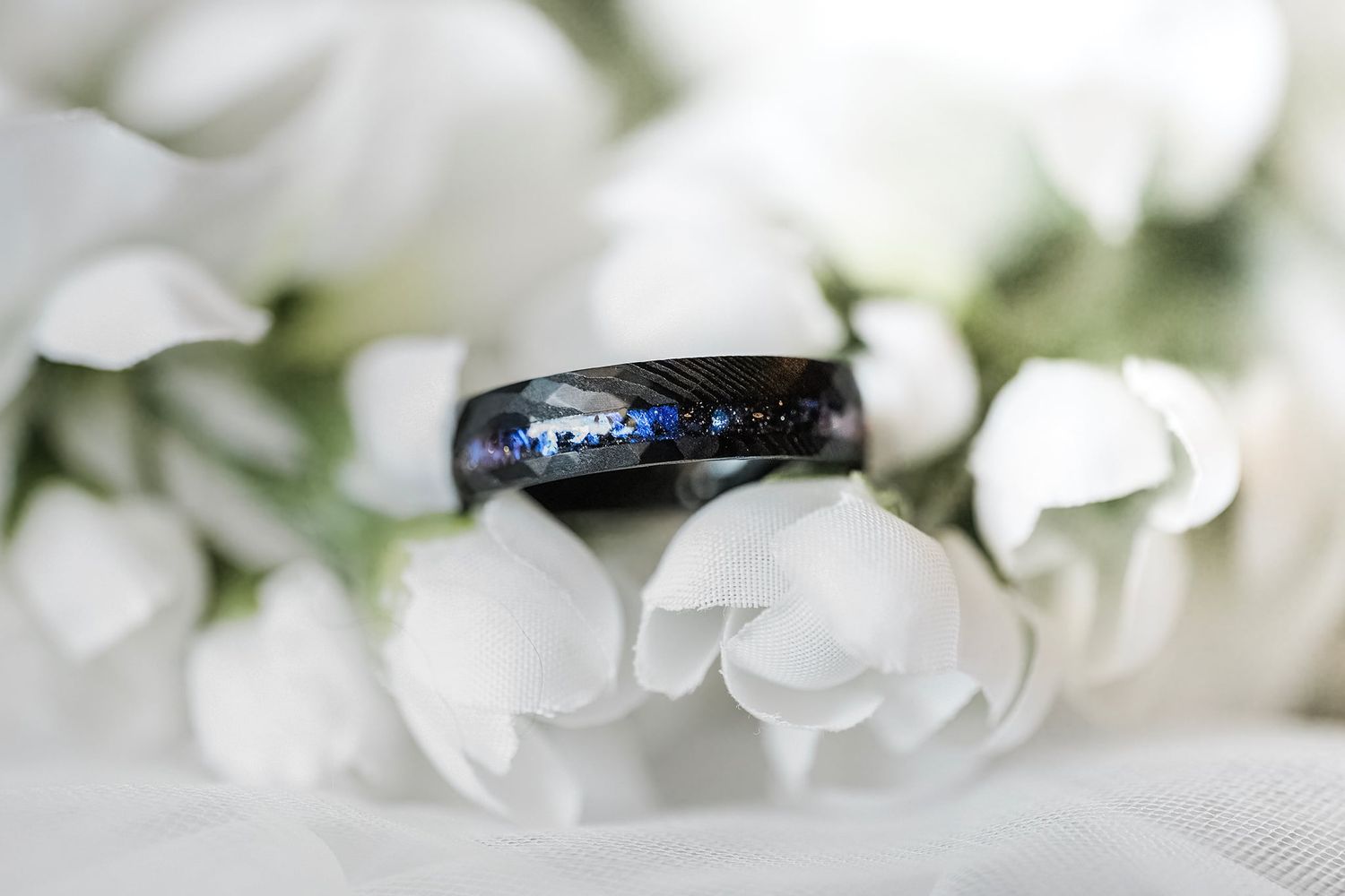 Elegant black tungsten wedding band with galaxy inlay resting on white floral bouquet.