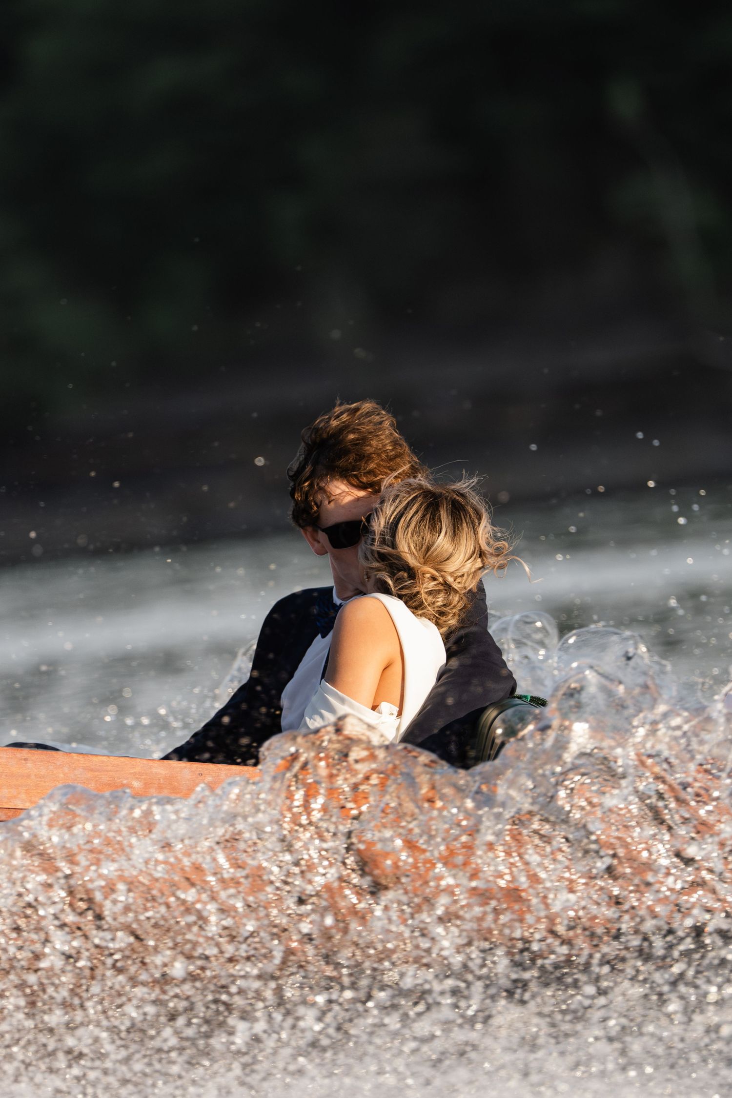 Couple embracing near splashing water fountain, woman in white dress and man in dark suit.