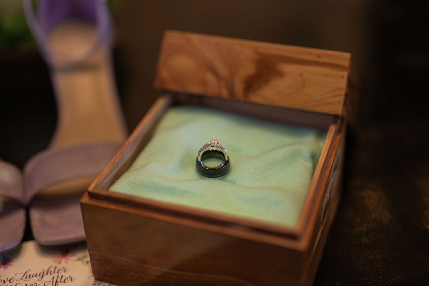 Diamond ring displayed in an open wooden jewelry box with green velvet lining on a dark surface.
