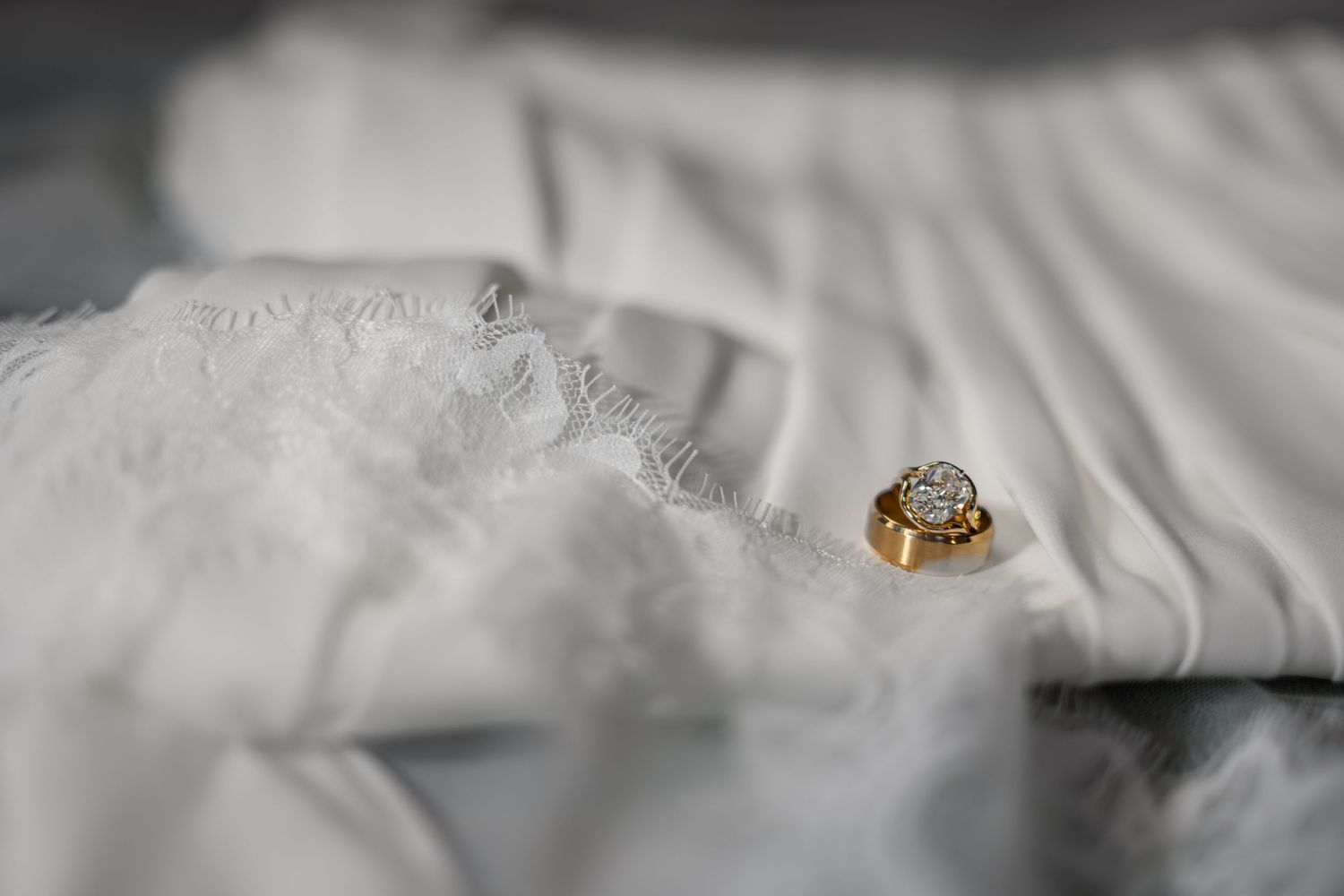 Gold diamond cluster ring resting on white lace wedding dress fabric in soft natural light.