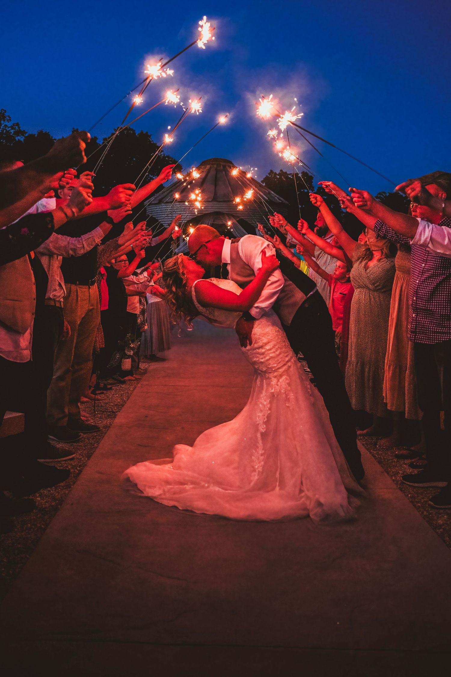 A groom dips his bride for a romantic kiss during a stunning sparkler exit at twilight.