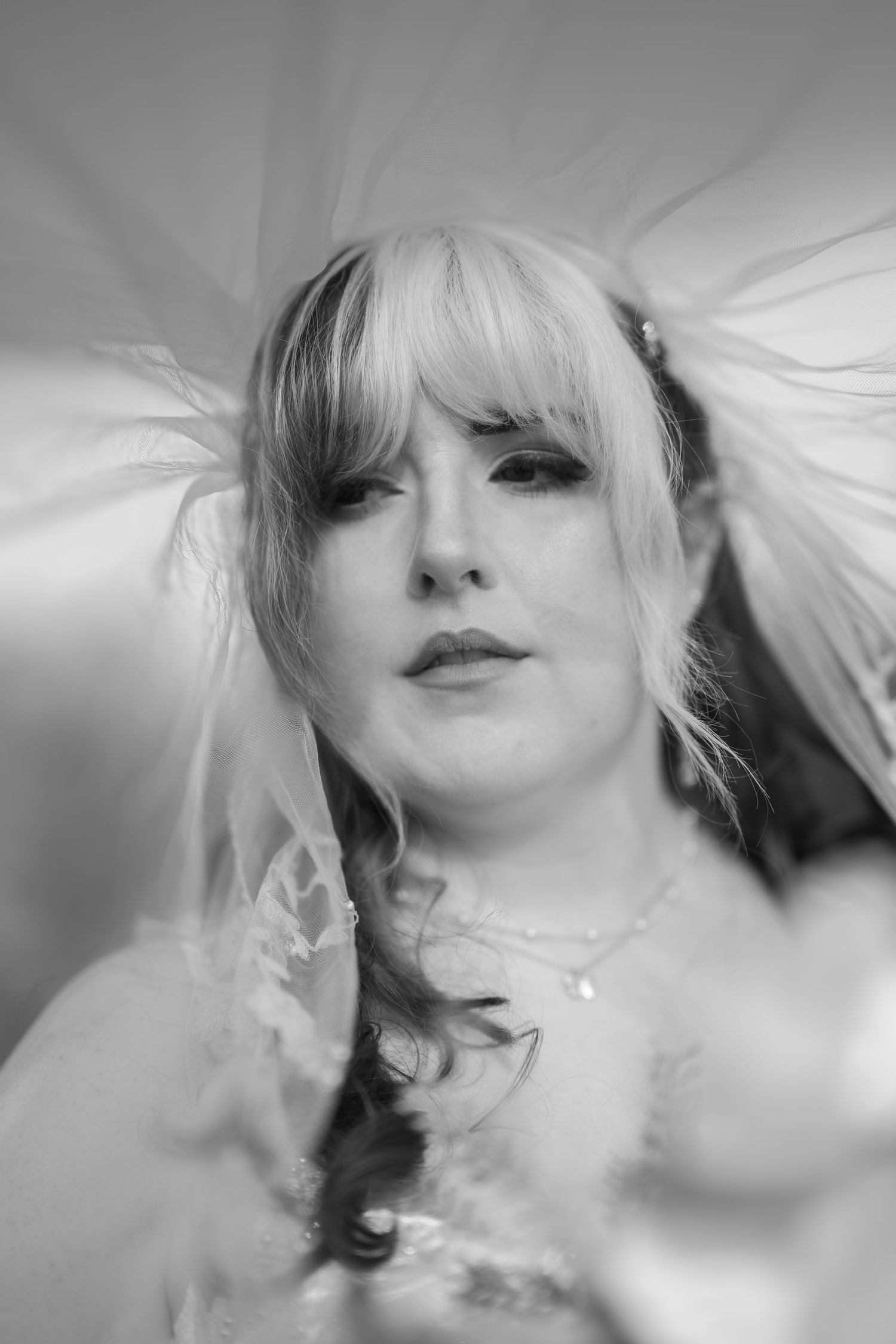 Black and white portrait of a bride wearing a veil and necklace, with dramatic eye makeup and blonde hair.