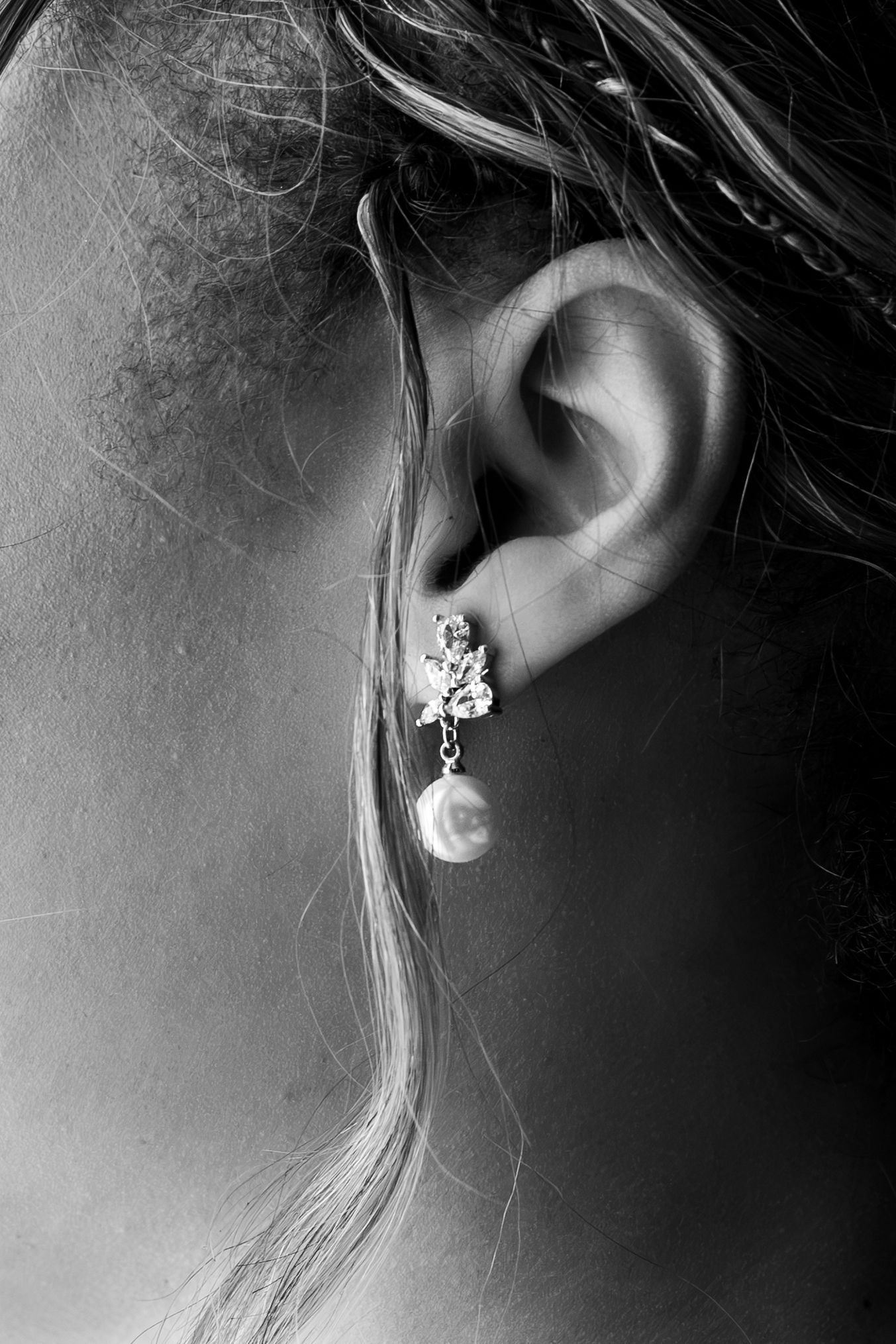 Black and white close-up of a woman's ear adorned with an elegant pearl and crystal drop earring.