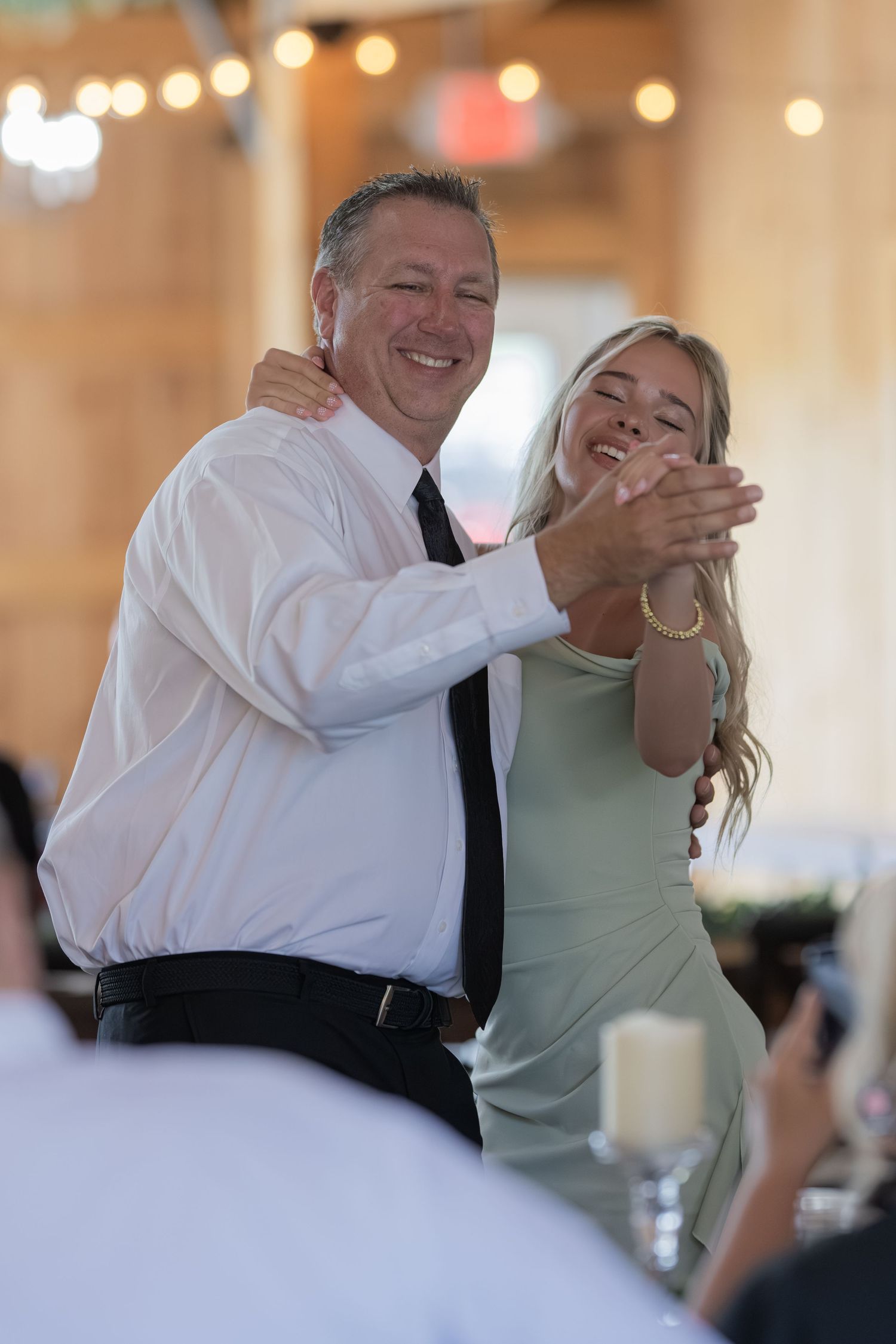 Father and daughter share a joyful dance together at rustic barn wedding reception under string lights.