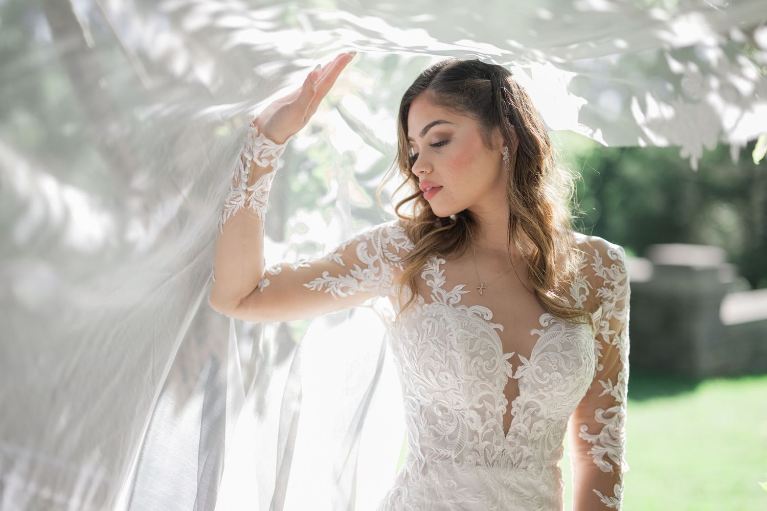 Bride in lace long-sleeve wedding gown holding flowing veil outdoors in soft natural light. Cheekwood. Nashville.