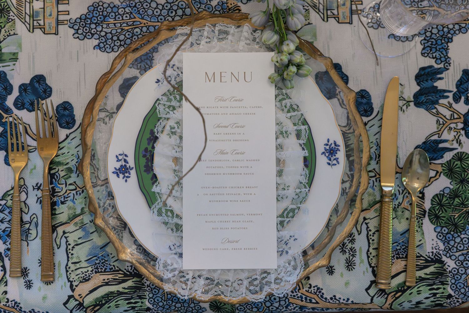 Elegant wedding place setting with gold flatware, ornate charger plate, and printed menu card.