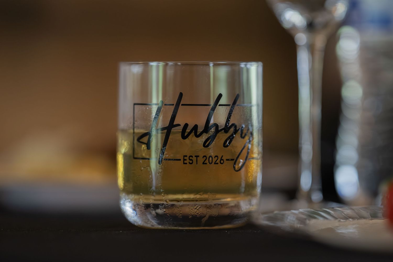Custom engraved whiskey glass with Stubbs EST 2026 design, filled with amber liquid on a table.