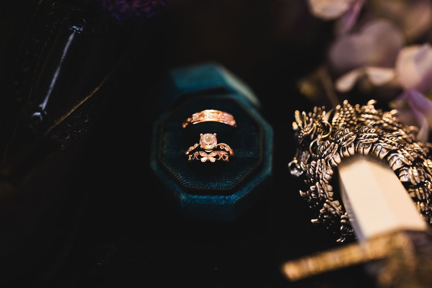 Gold engagement ring with diamond solitaire displayed in a dark velvet octagonal ring box with floral accents.