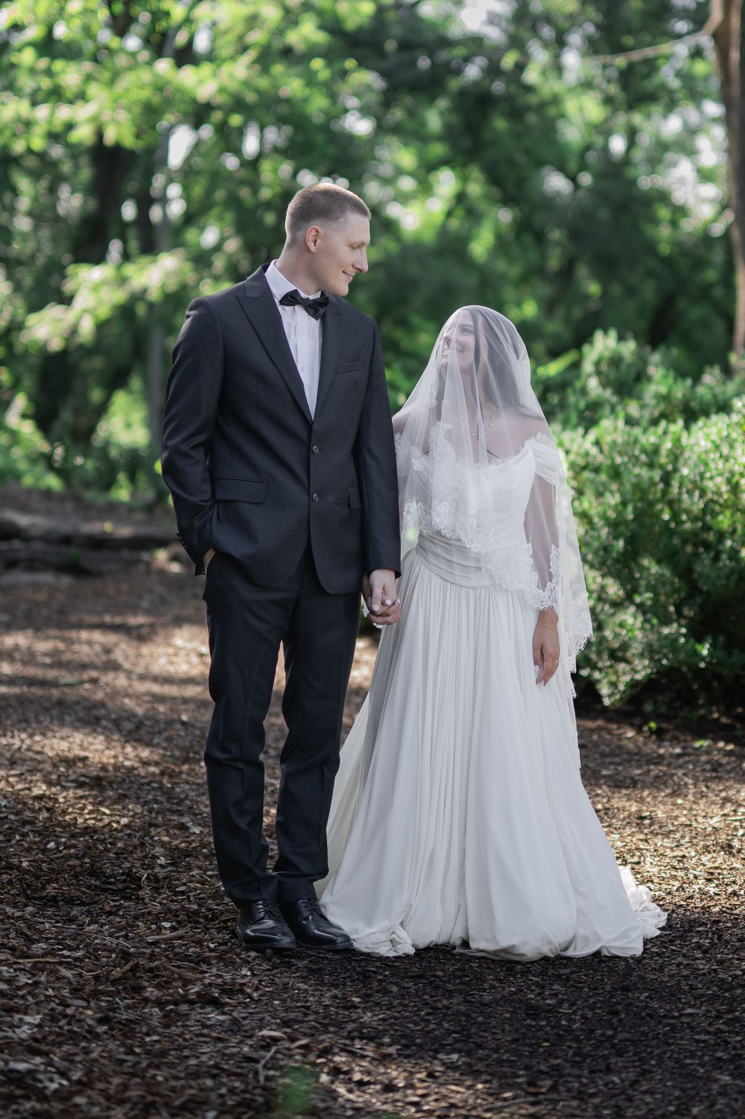Bride and groom holding hands walking through a lush green forest path on their wedding day.