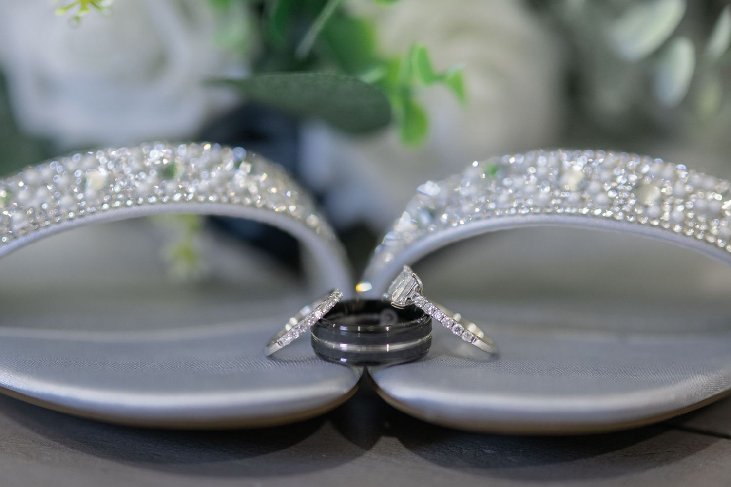 Silver beaded wedding sandals with diamond rings resting between them on a gray surface.