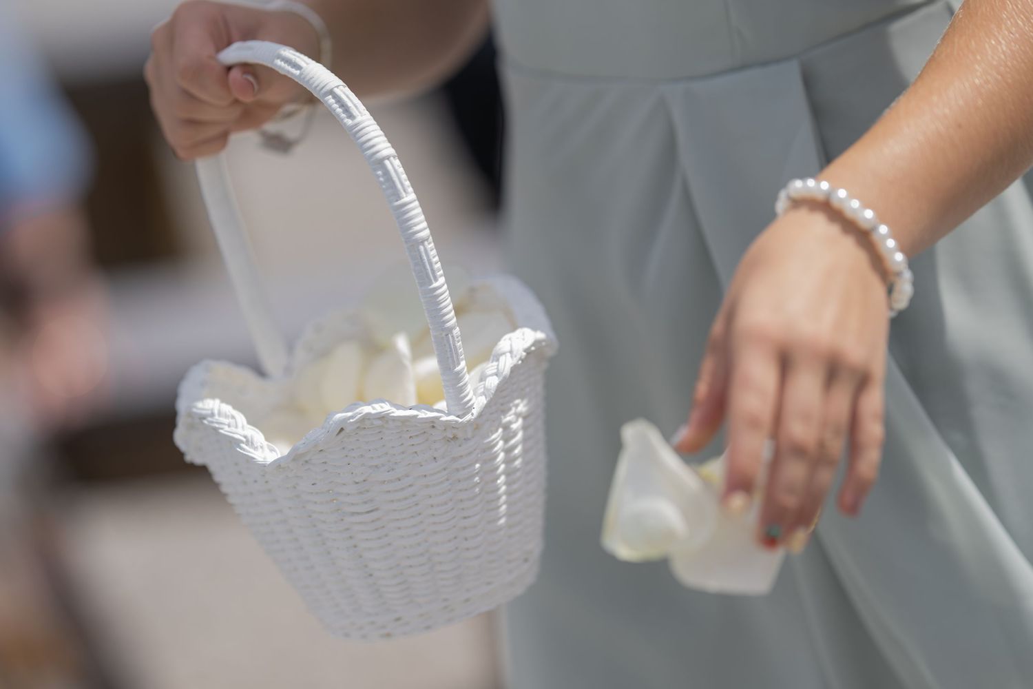 Bridesmaid holding a white wicker flower girl basket with pearl bracelet at a wedding ceremony.
