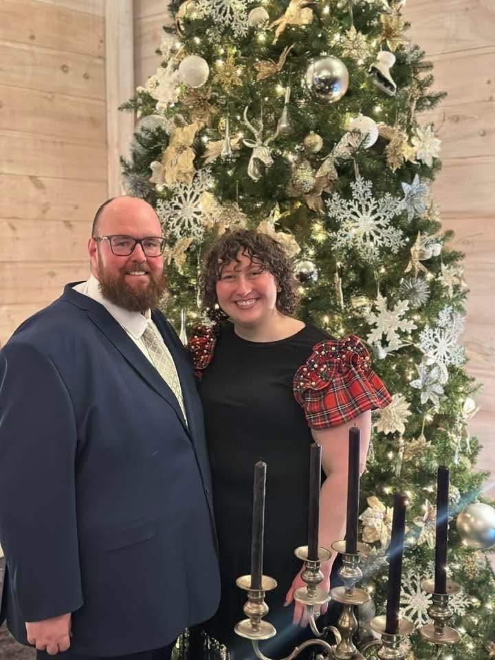 Couple smiling together in front of decorated Christmas tree with snowflake ornaments and candlesticks.