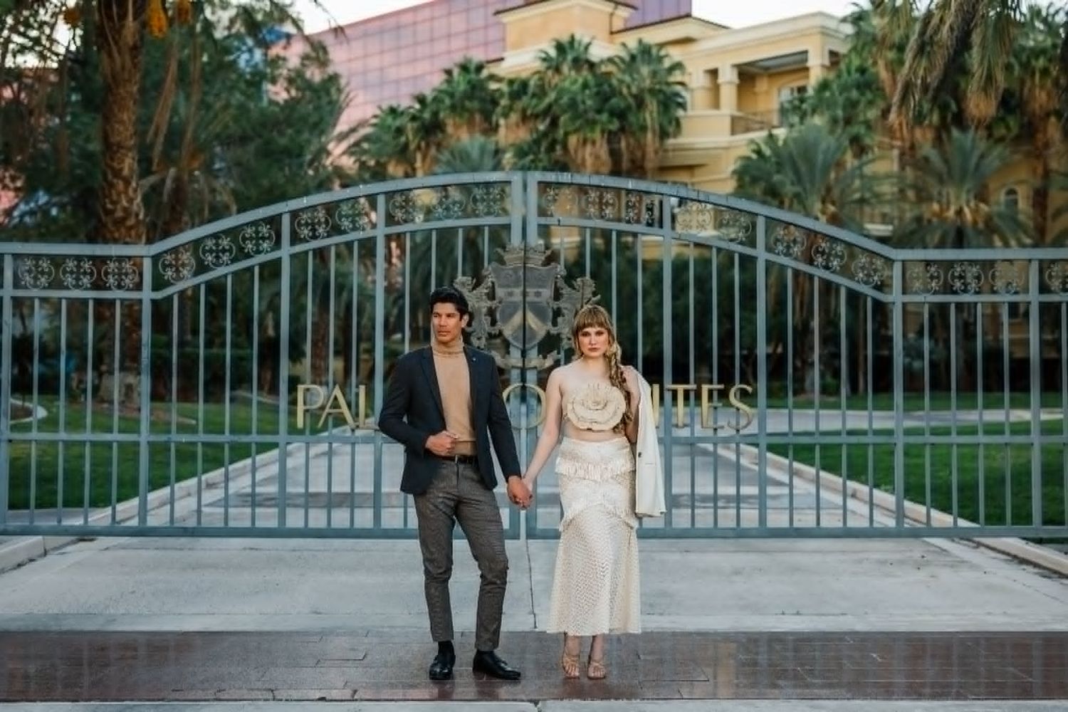 Couple holding hands in front of ornate iron gates at Paris Las Vegas, bride in white dress and groom in suit.