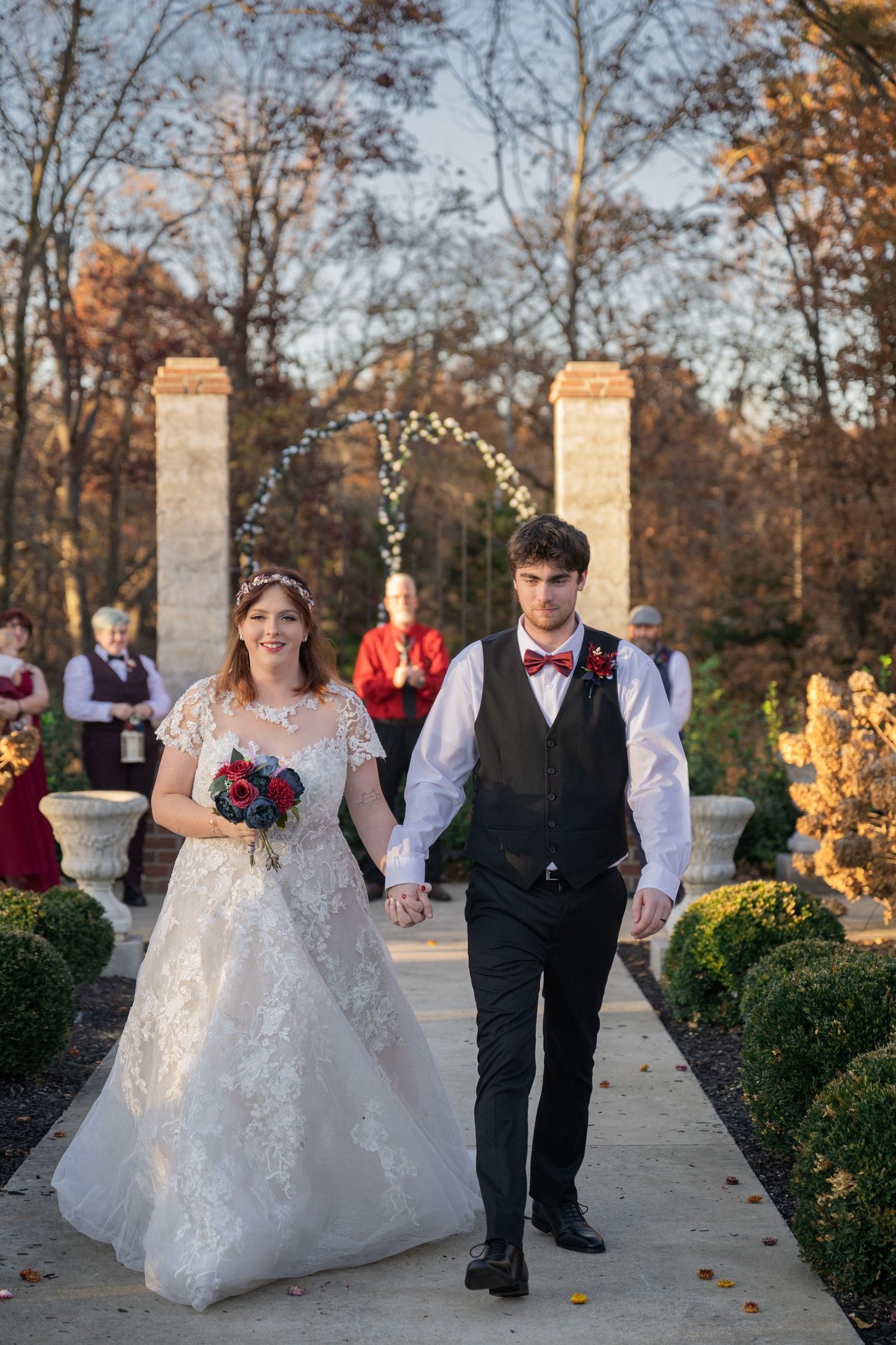 Newlywed couple walking hand in hand down a garden aisle at golden hour after their outdoor ceremony.