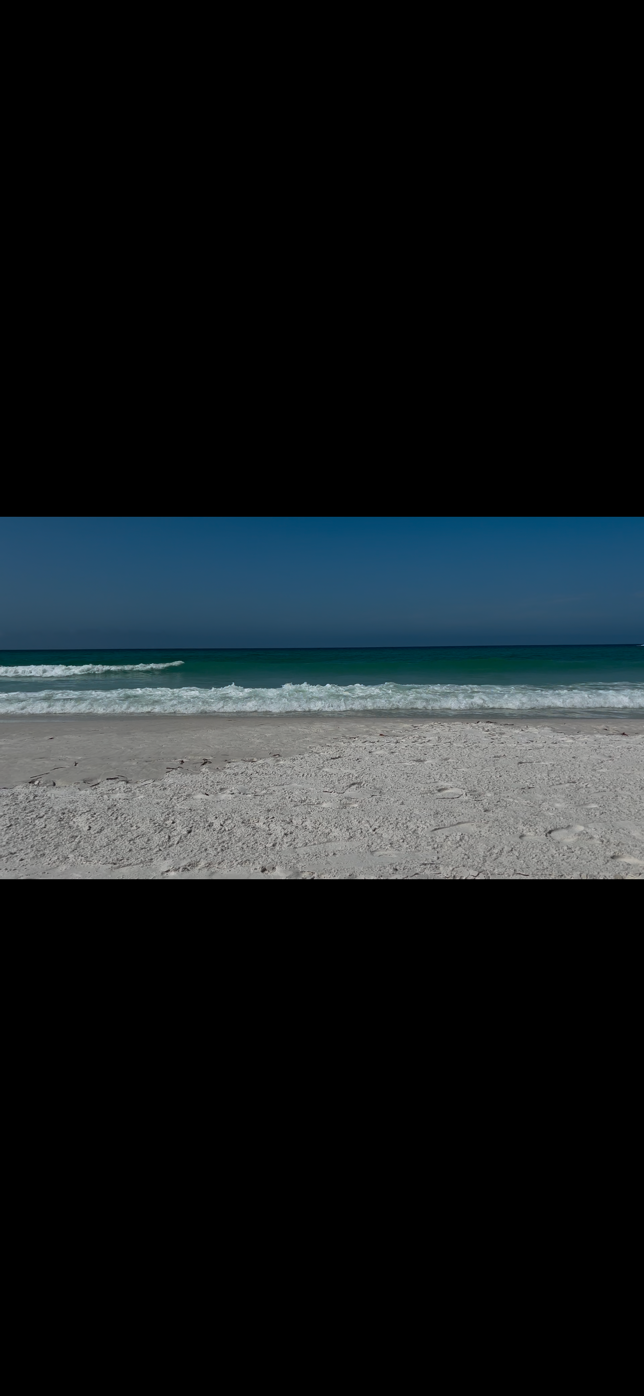 White sandy beach with turquoise ocean waves under a clear blue sky on a sunny day.