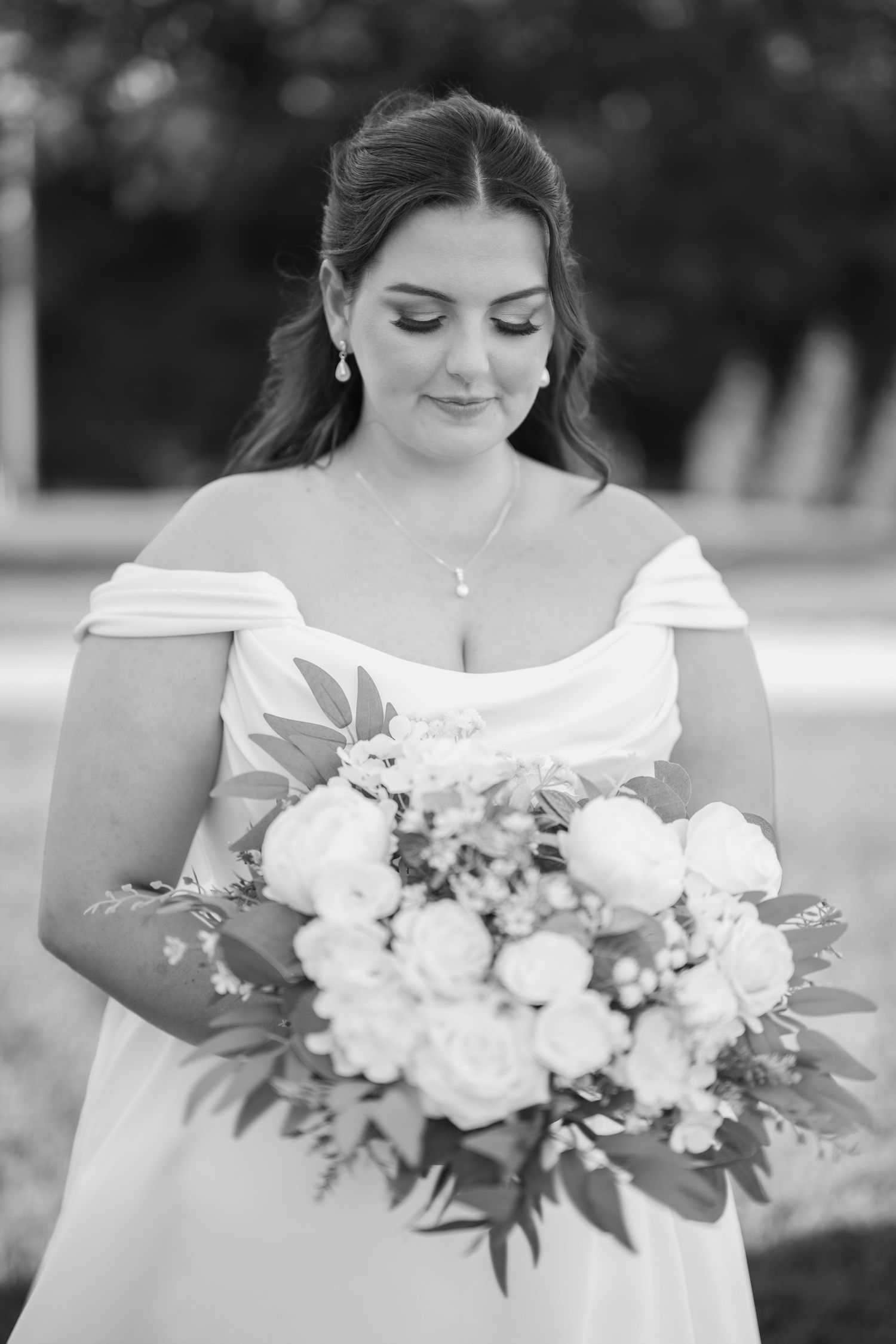 Black and white bridal portrait of a woman in an off-shoulder gown holding a bouquet of white peonies and greenery.