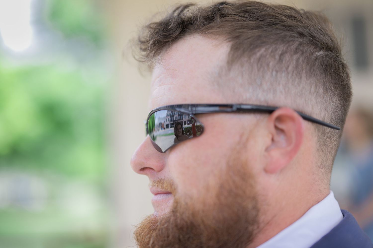 Bearded man wearing reflective sport sunglasses in profile view at an outdoor event.