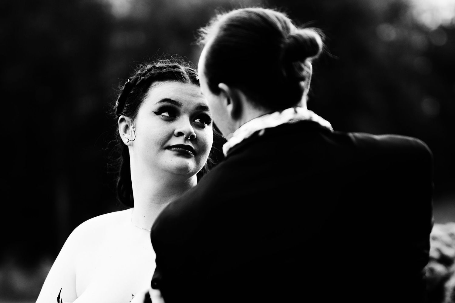 Black and white wedding photo of bride smiling at groom during outdoor ceremony.