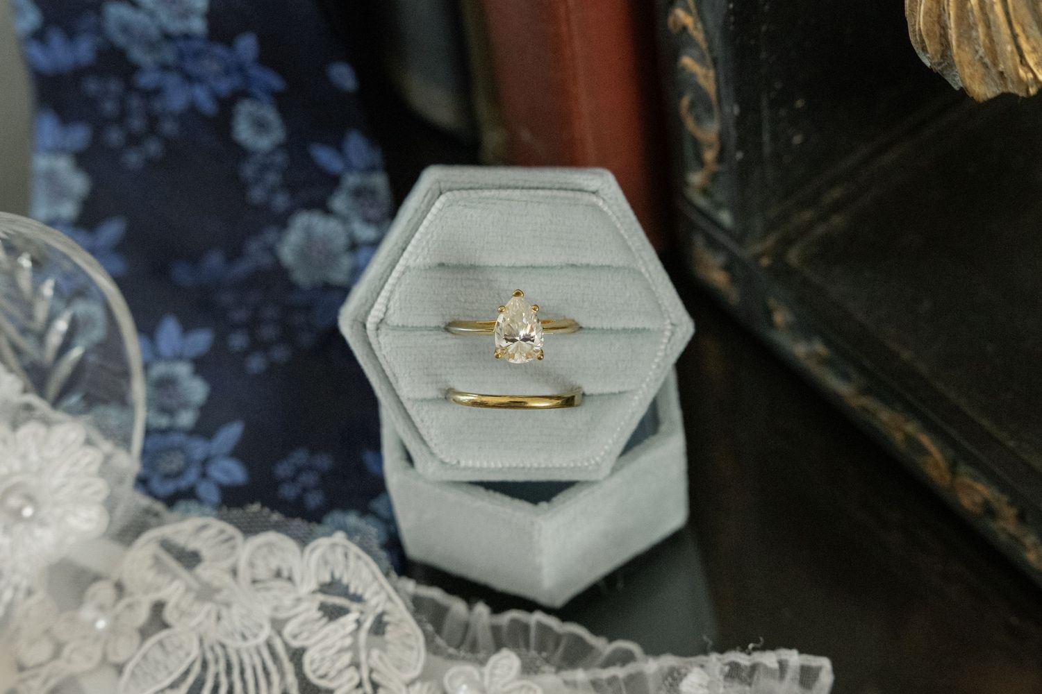 Gold pear-shaped diamond engagement ring displayed in a gray velvet hexagon ring box.