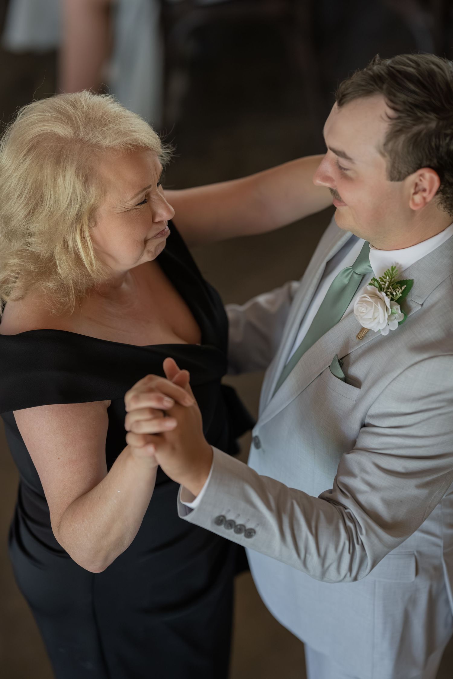 Groom in gray suit dancing with mother at wedding reception in heartfelt mother-son dance.