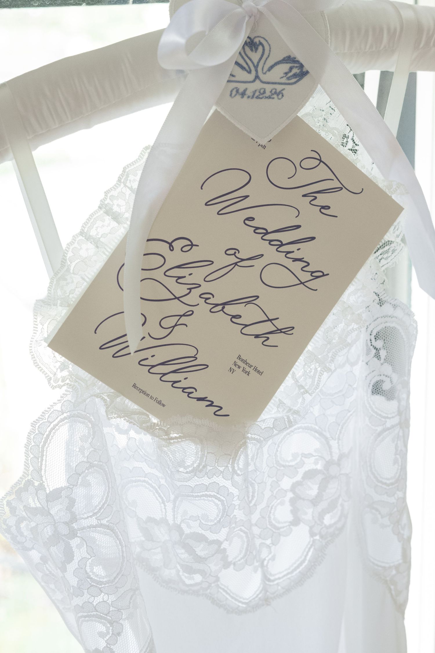Elegant wedding program card with calligraphy script reading The Wedding of Elizabeth and William, displayed on a lace bridal gown.