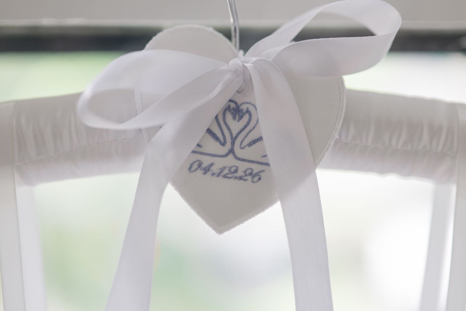 White wedding hanger with satin bow and custom date tag reading 04.12.25 featuring swan logo design.