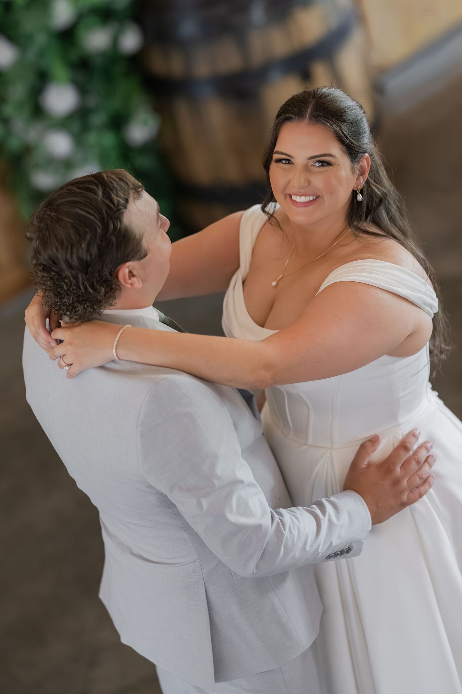 Bride in white gown smiles joyfully at groom during first dance at elegant wedding reception.