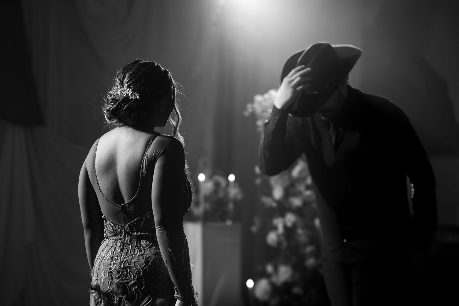 Black and white wedding photo of bride in backless gown and groom bowing emotionally on stage.