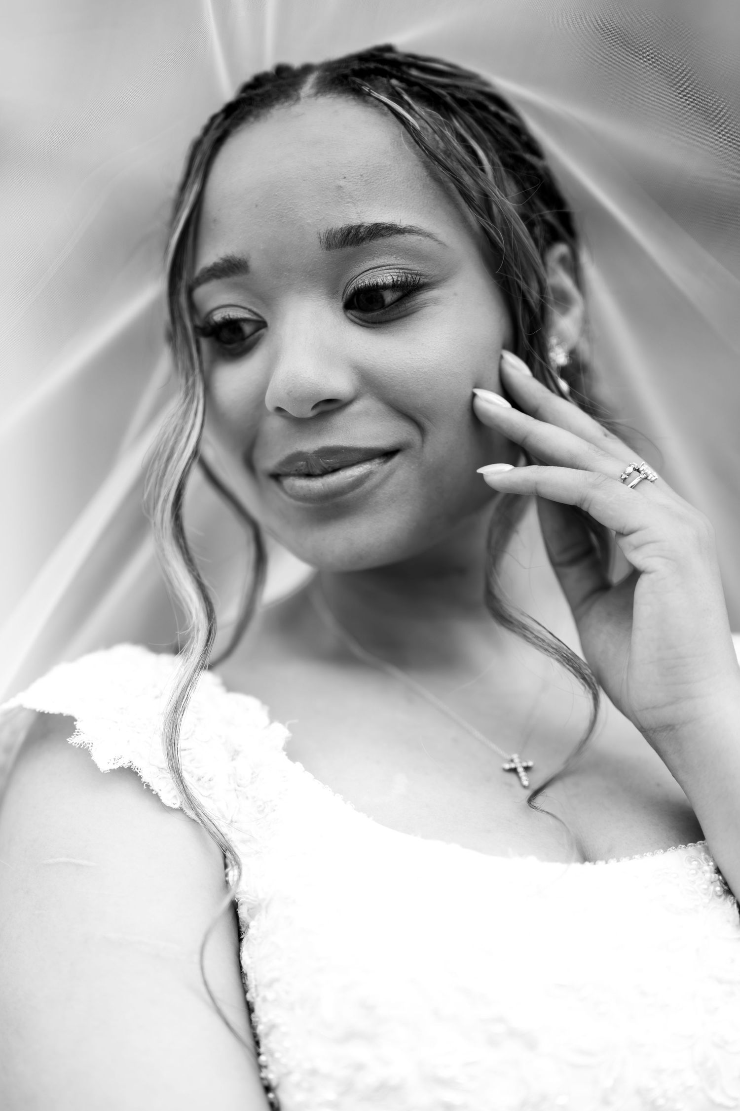 Black and white portrait of a bride in a white dress and veil, wearing a cross necklace and ring, smiling softly.