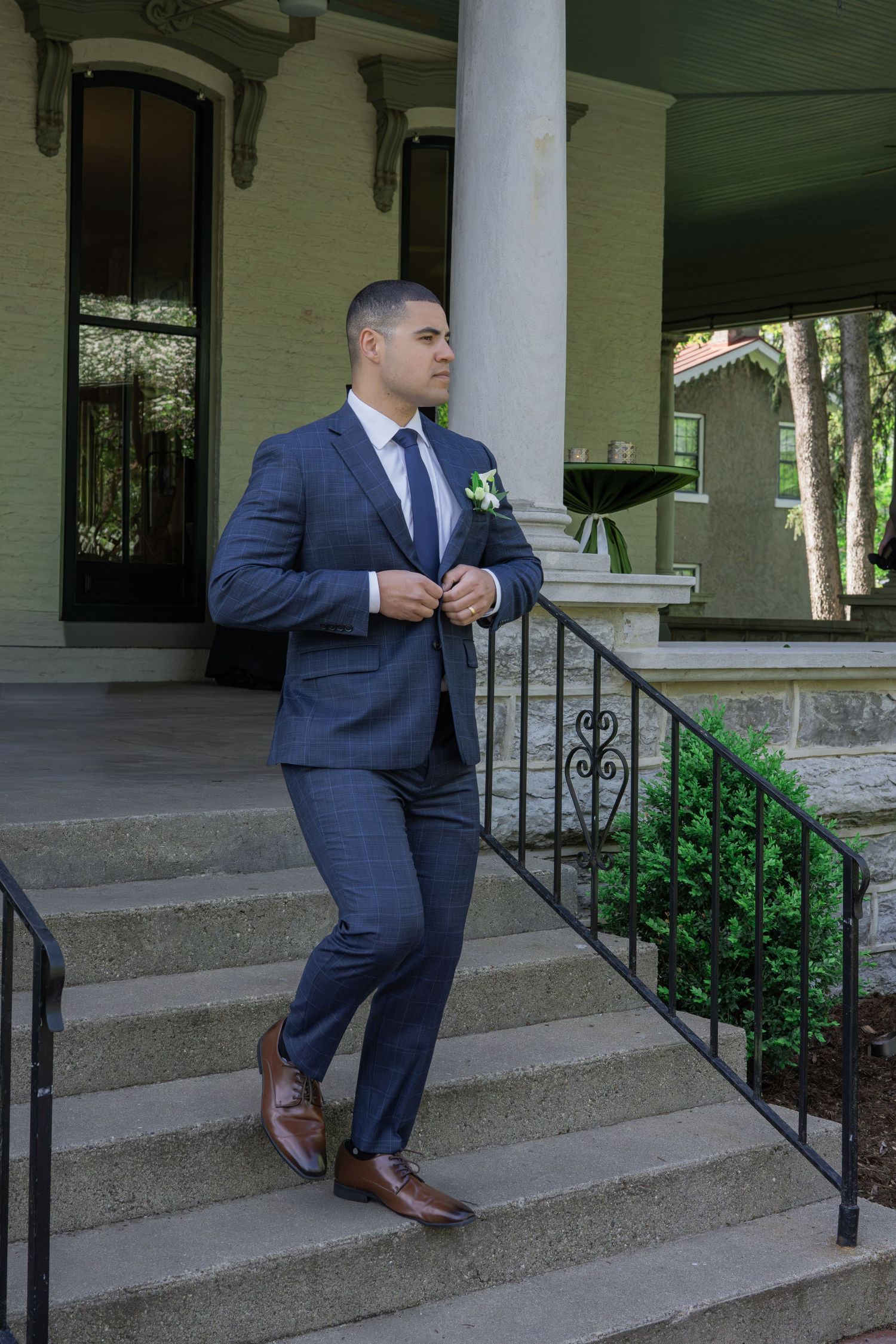 A groom in a navy blue suit with boutonniere poses on stone steps outside an elegant venue.
