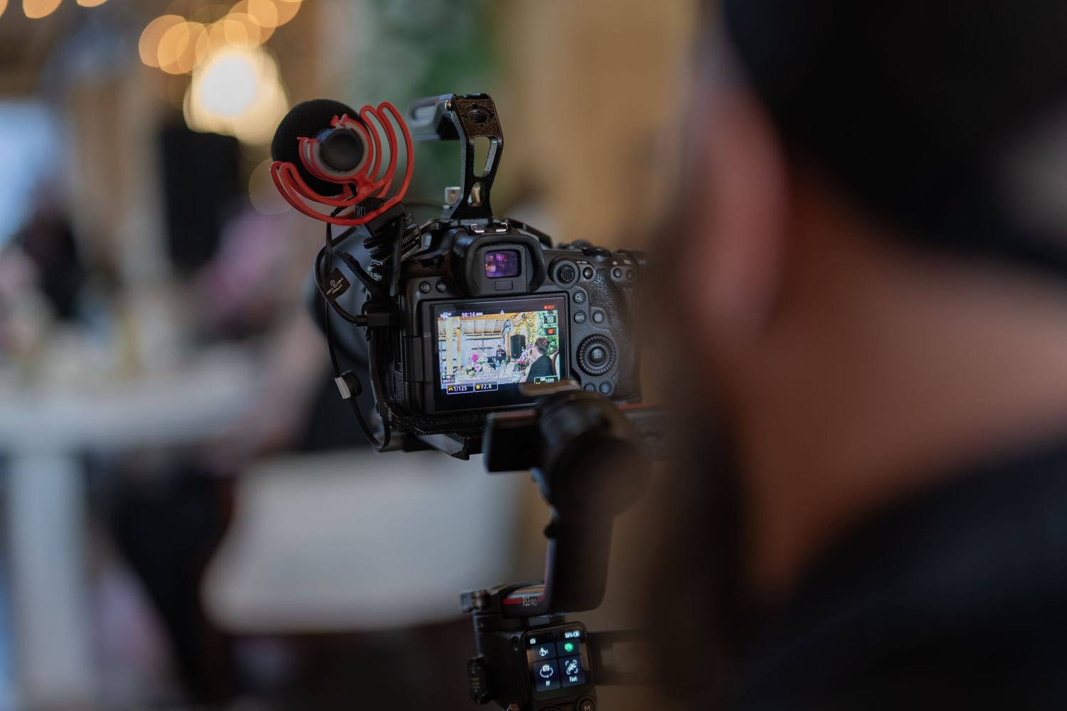A videographer films an event using a DSLR camera with a red microphone mounted on a stabilizer gimbal.
