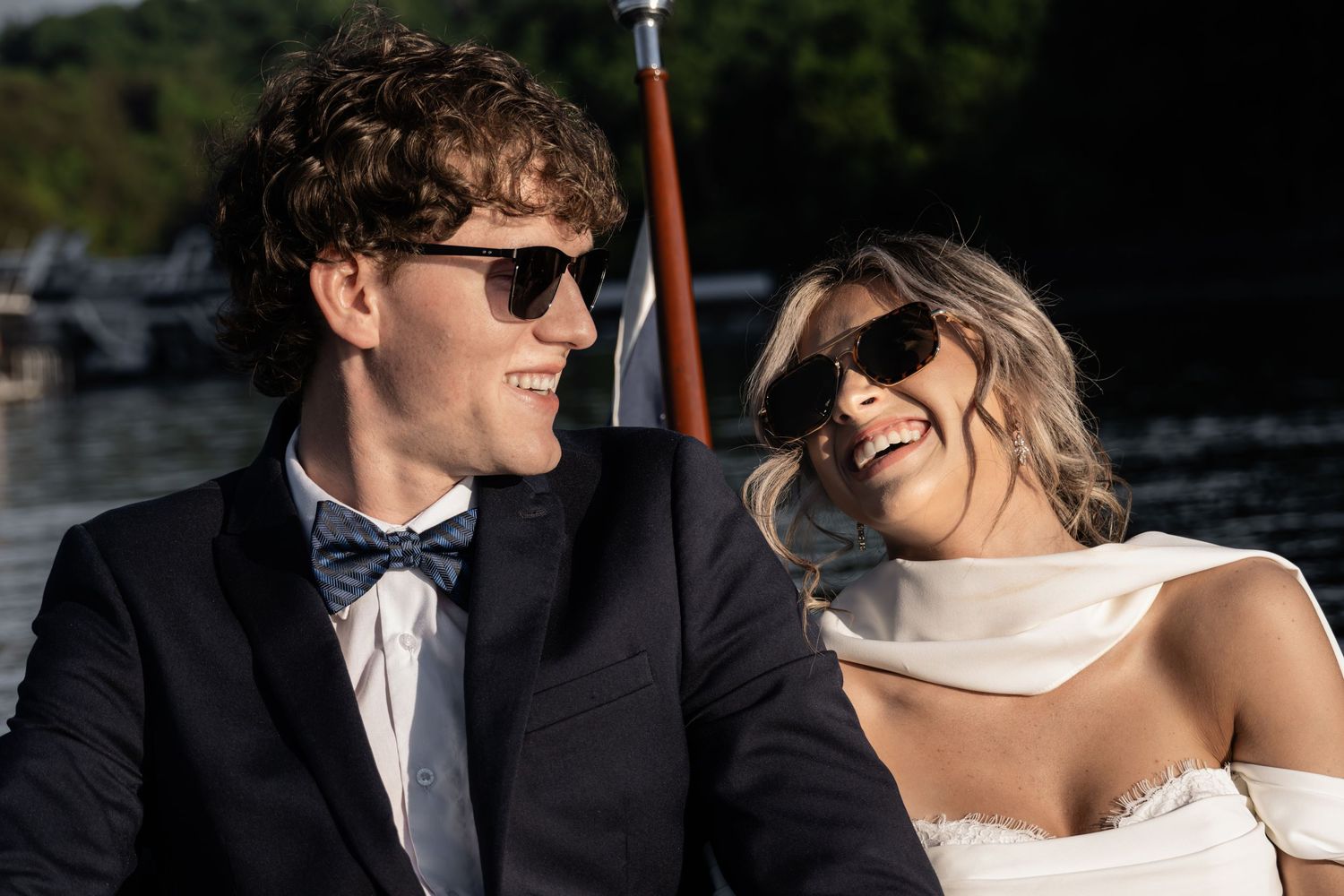 Smiling bride and groom in sunglasses sharing a joyful moment on a boat on their wedding day.