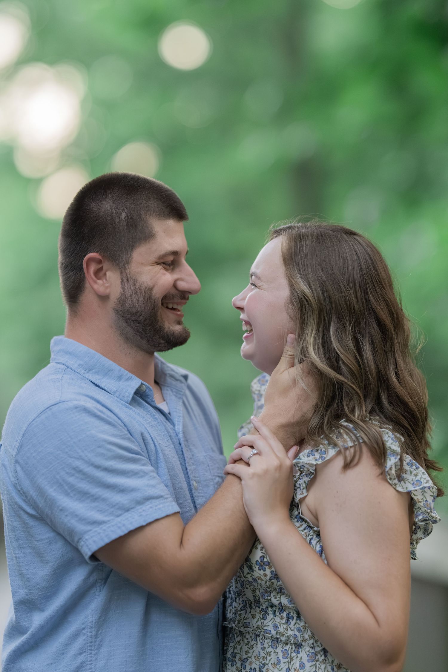 A smiling couple holds hands and laughs together outdoors in a lush green park during golden hour.