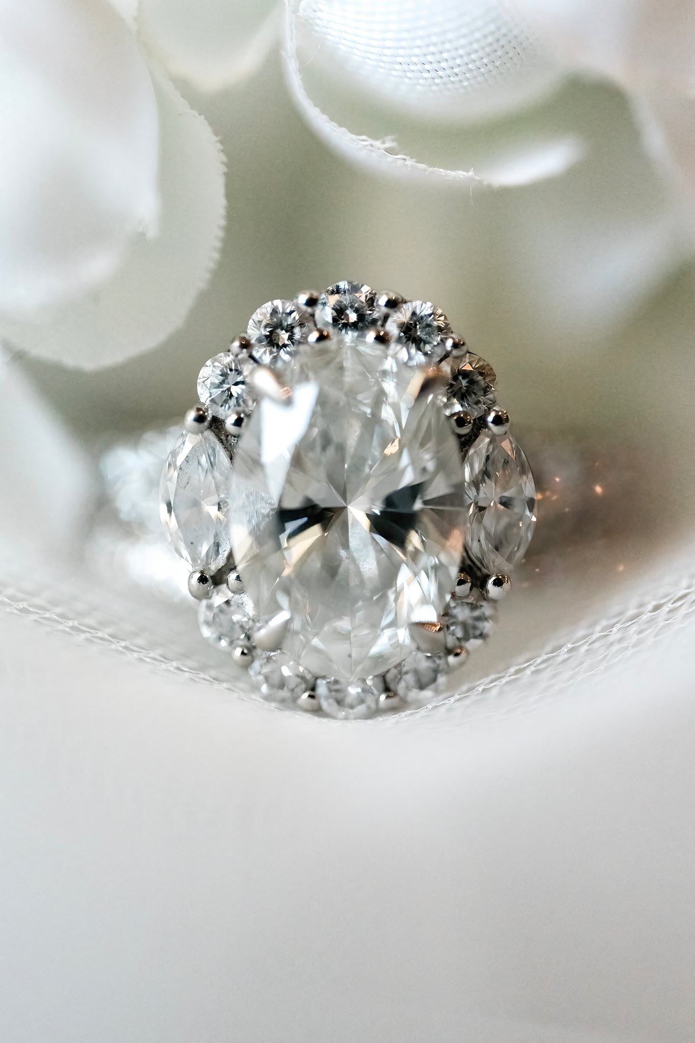 Oval diamond halo engagement ring displayed on white fabric background.