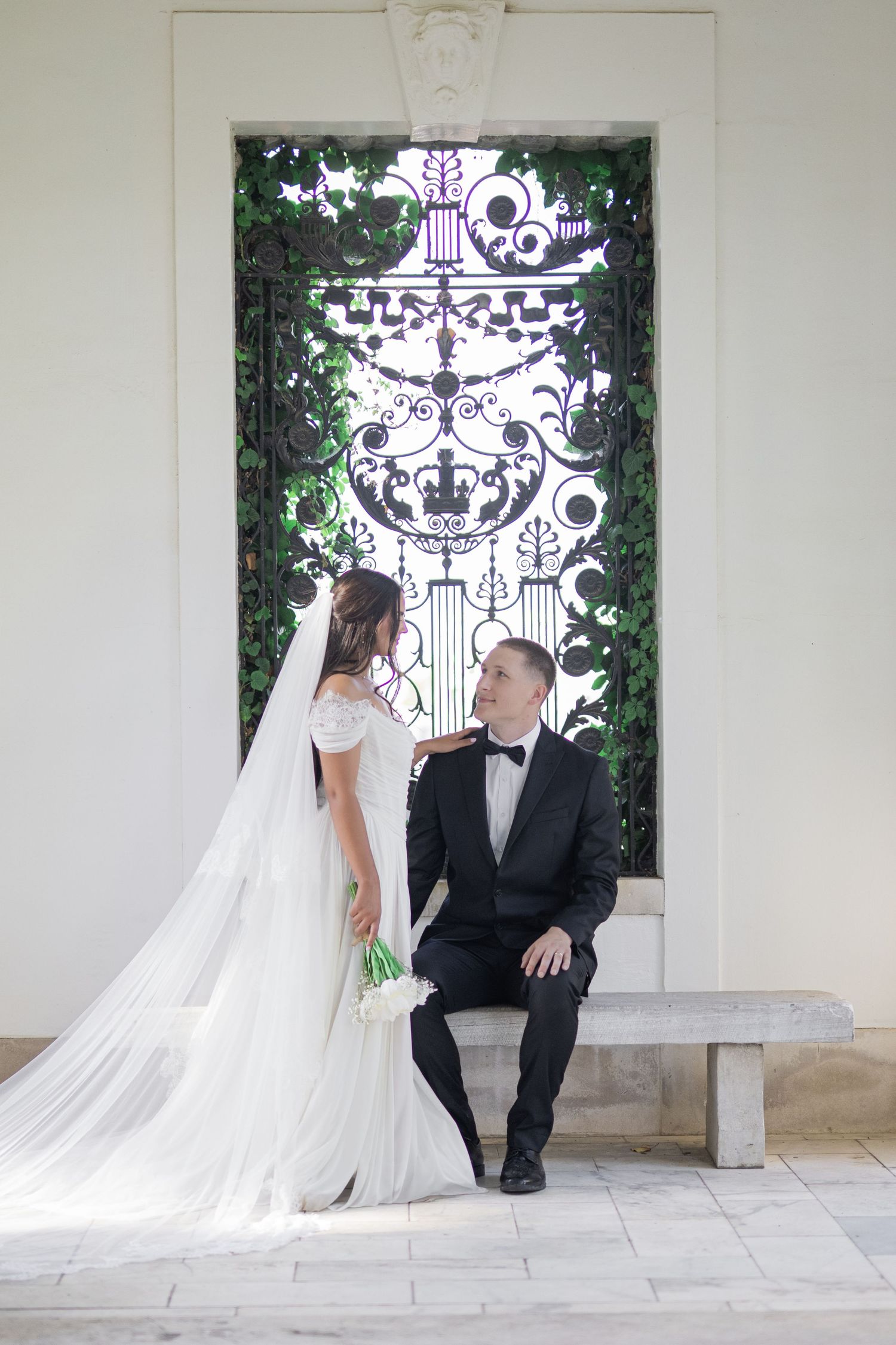 Cheekwood. Nashville. Bride in white gown with veil and groom in black tuxedo posing before ornate iron gate with ivy.
