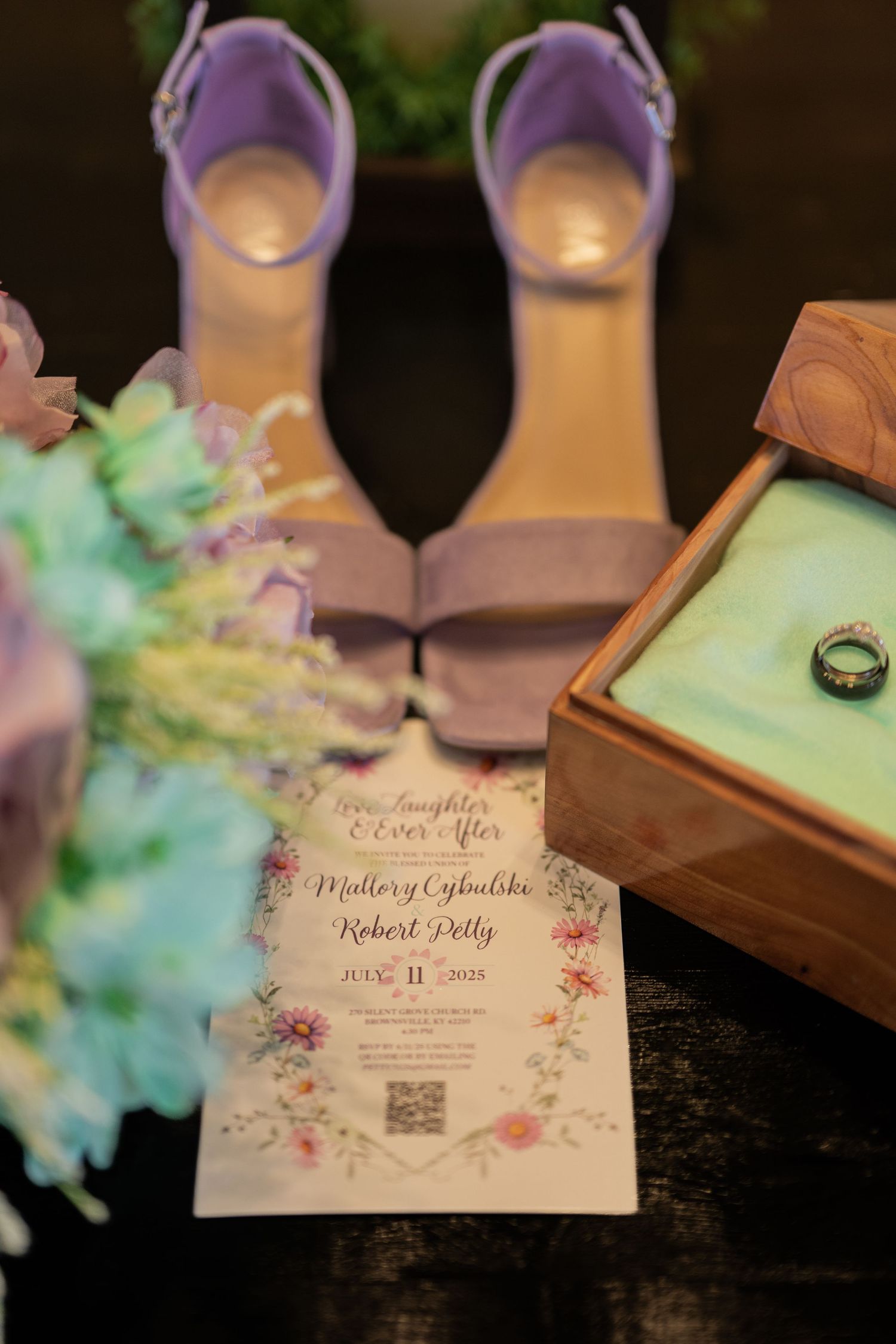 Wedding flat lay featuring invitation for Mallory Cybulski and Robert Petty, lavender heels, floral bouquet, and ring box.