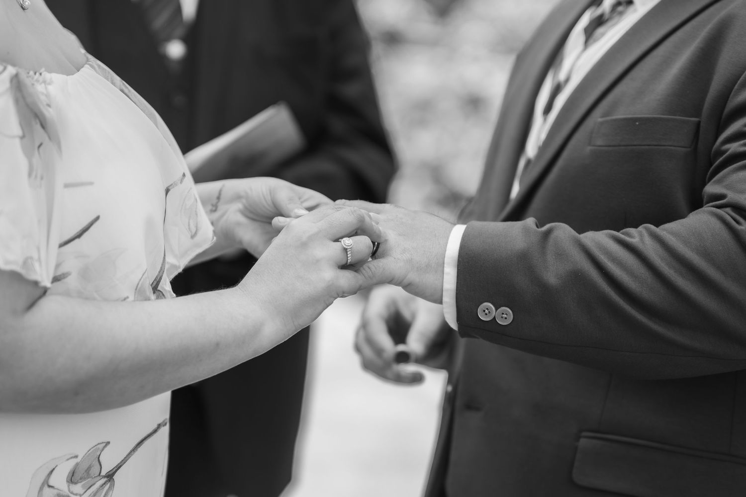 Black and white photo of a bride placing a wedding ring on the groom's finger during a wedding ceremony.