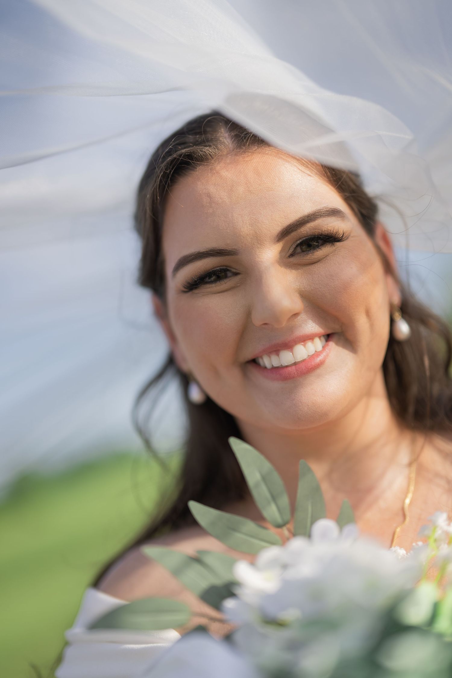 Smiling bride in white veil holding bouquet of white flowers and greenery on her wedding day.