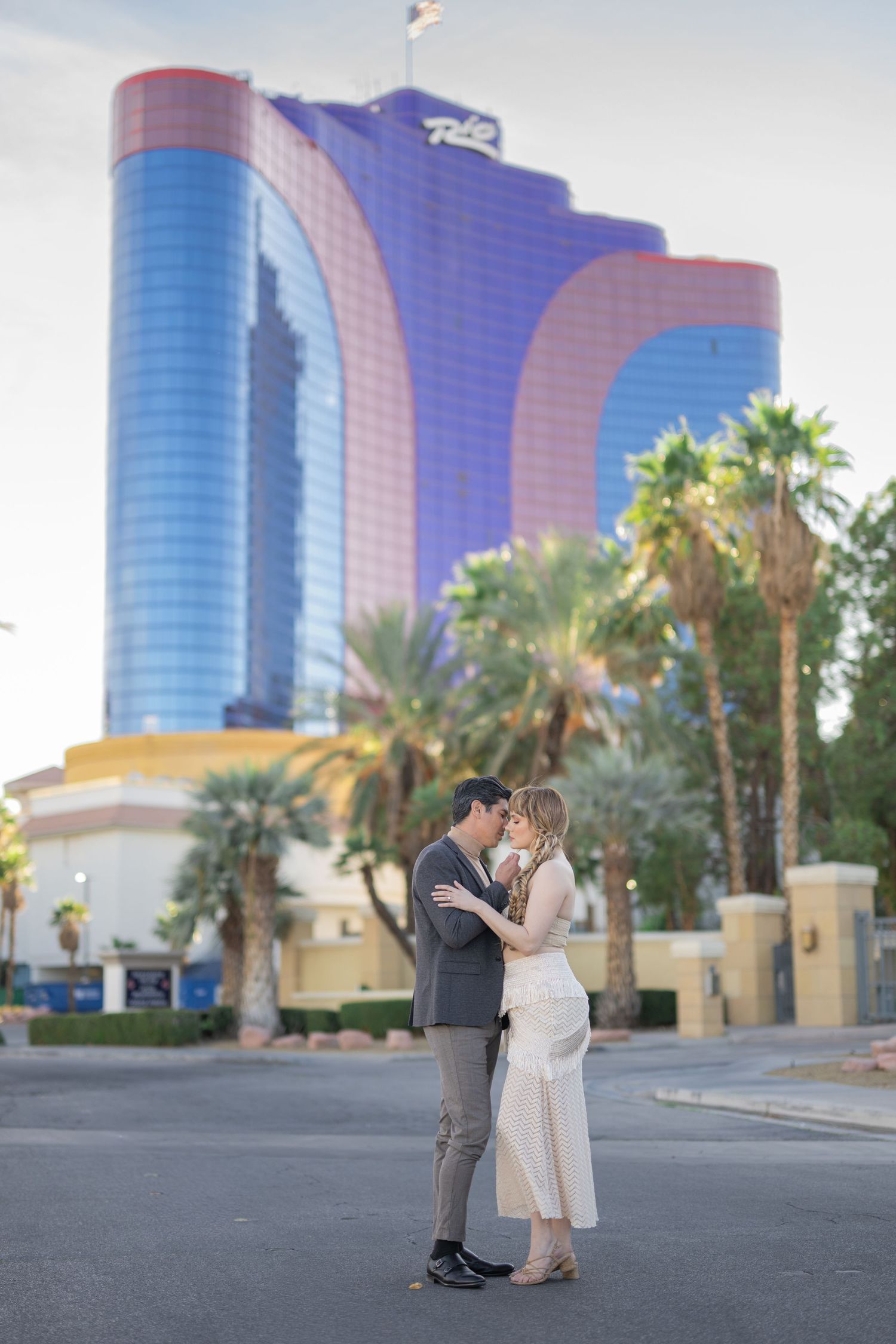 Couple kissing in front of the Rio Hotel and Casino in Las Vegas with palm trees backdrop.