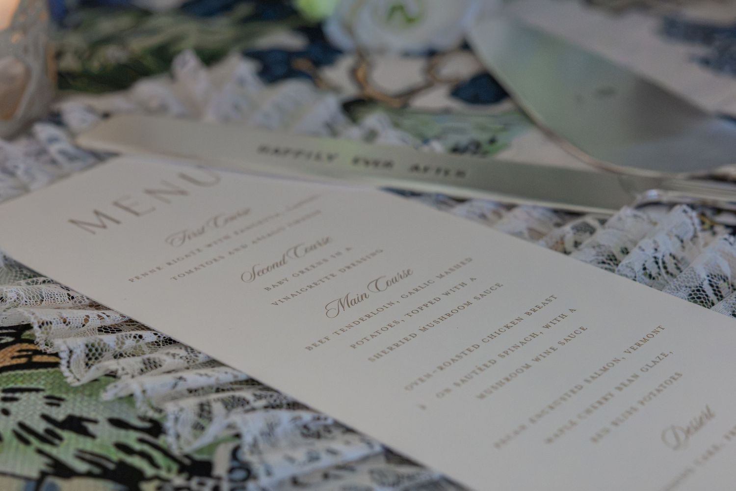 Elegant wedding reception menu card displayed on a lace tablecloth with floral decorations in the background.