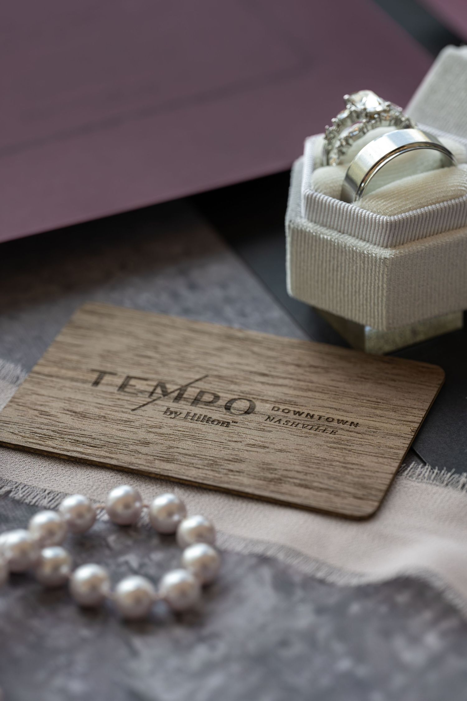 Tempo by Hilton Downtown key card beside pearl bracelet and silver wedding rings in a white jewelry box.