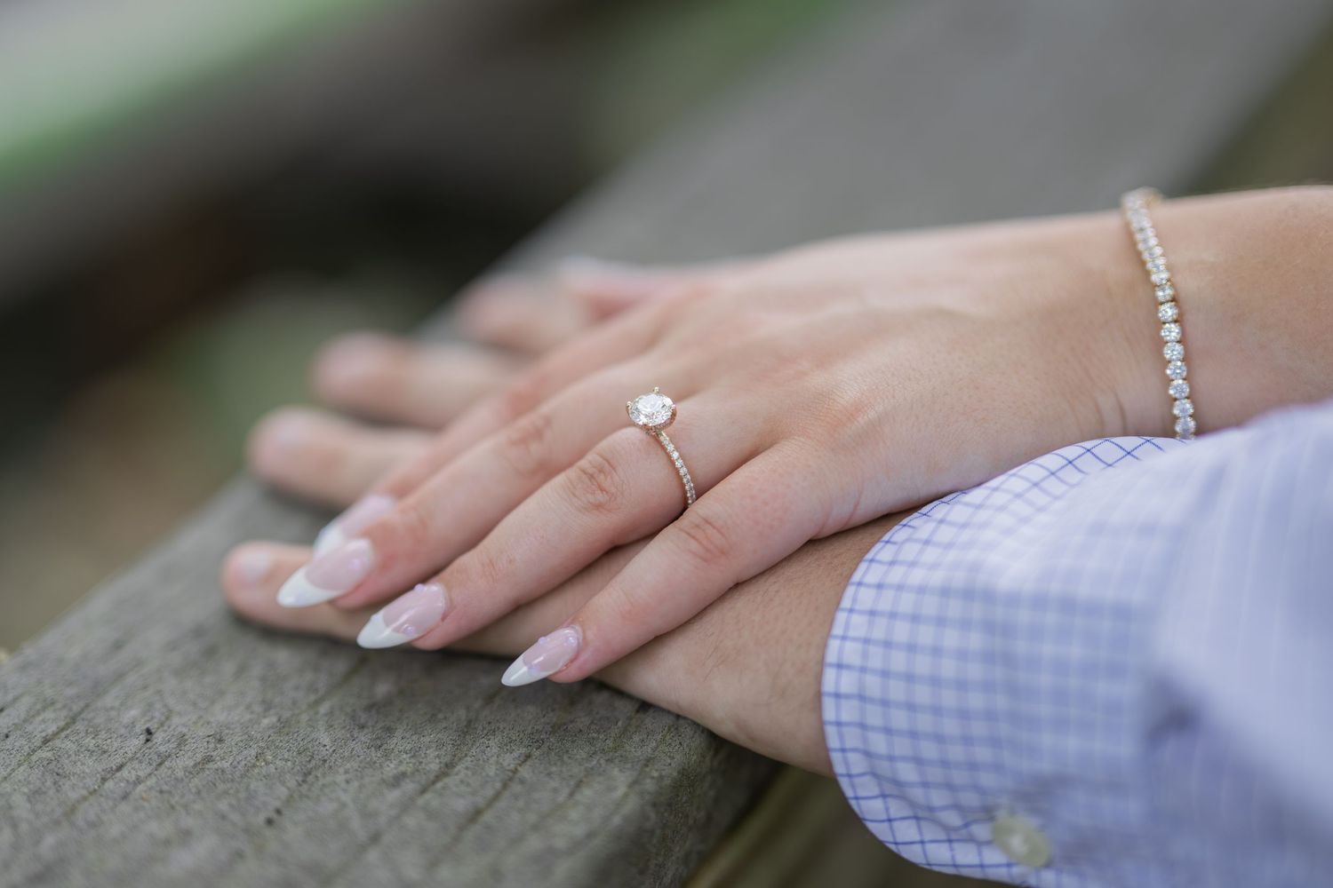 Close-up of a woman's hand wearing a diamond engagement ring and pearl bracelet, resting on a wooden surface.