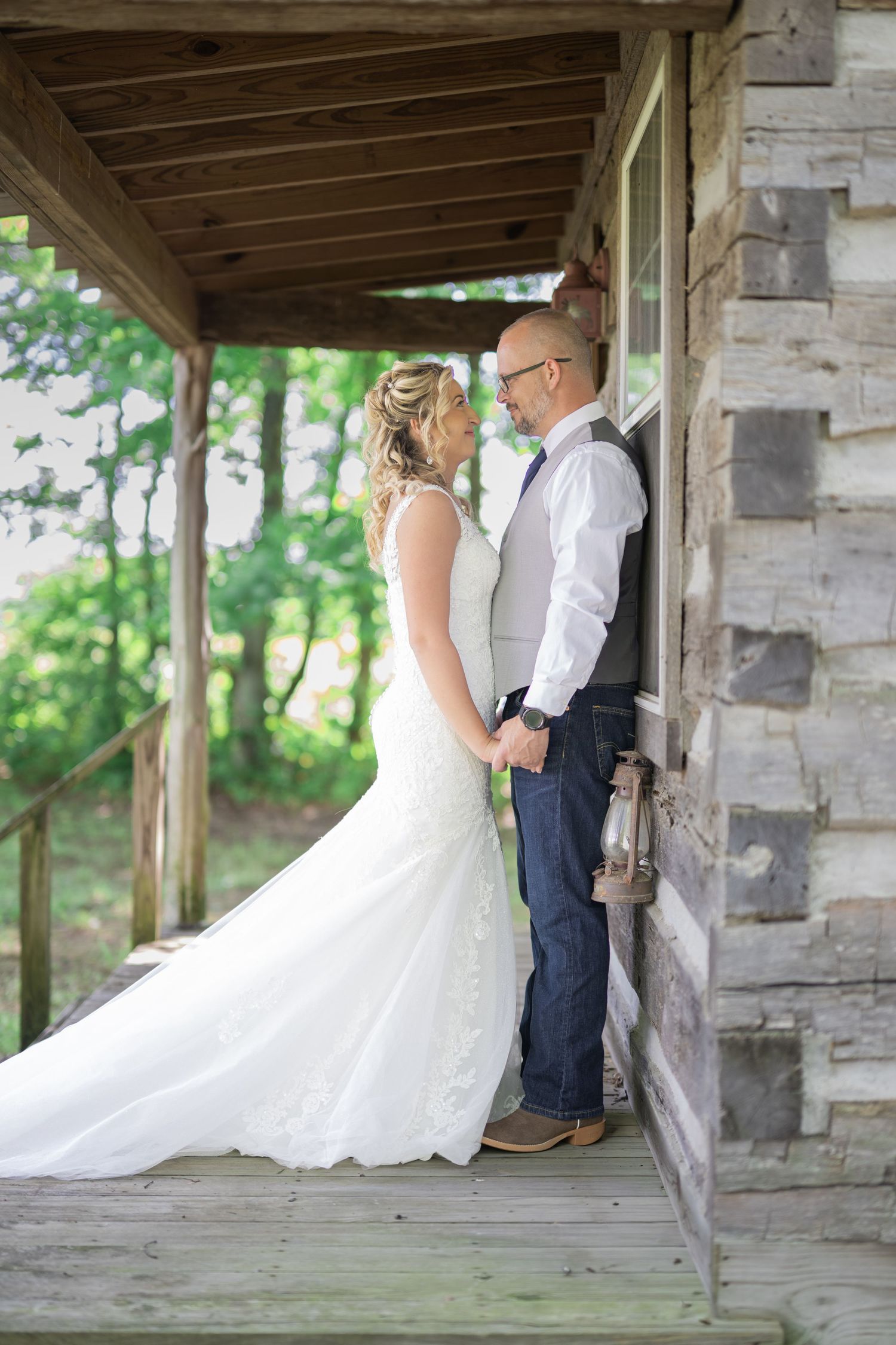 Bride and groom holding hands on rustic log cabin porch, sharing an intimate moment in wedding attire.