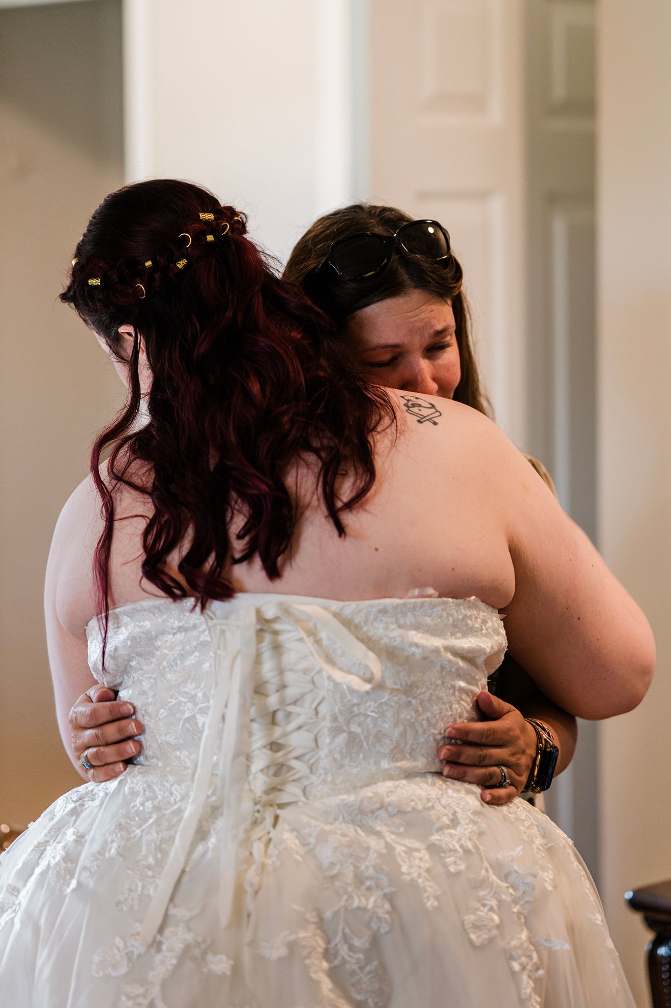 Two women embracing in an emotional hug, one wearing a white strapless wedding gown with lace details.