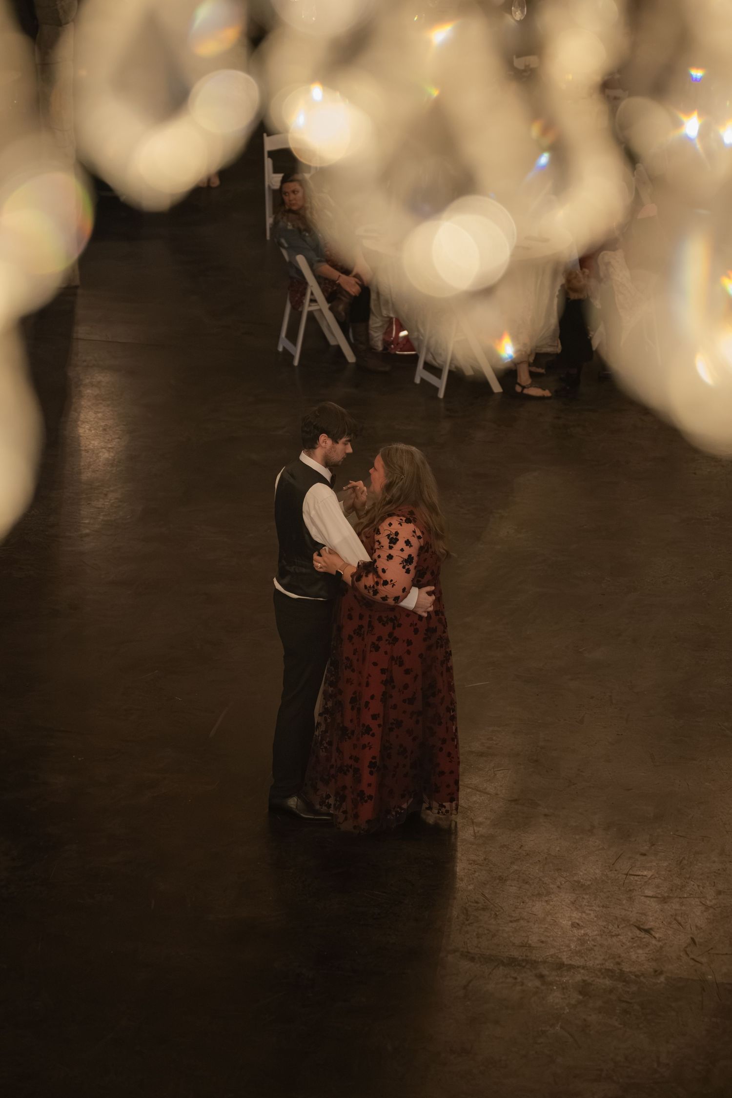 Couple shares romantic first dance on dark floor surrounded by glowing bokeh lights at elegant wedding reception.