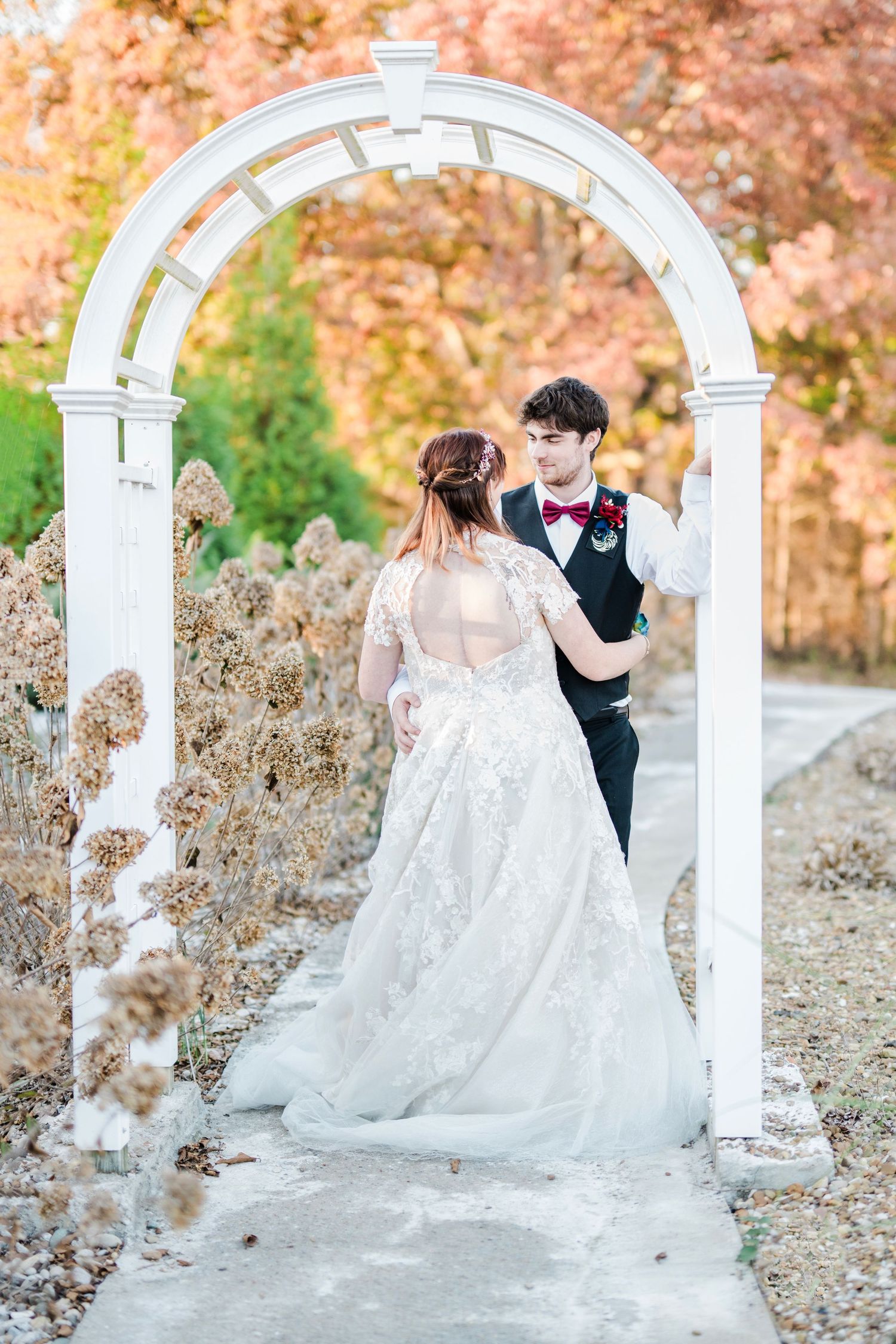 Bride and groom dancing under a white garden arch surrounded by autumn foliage in an outdoor wedding setting.