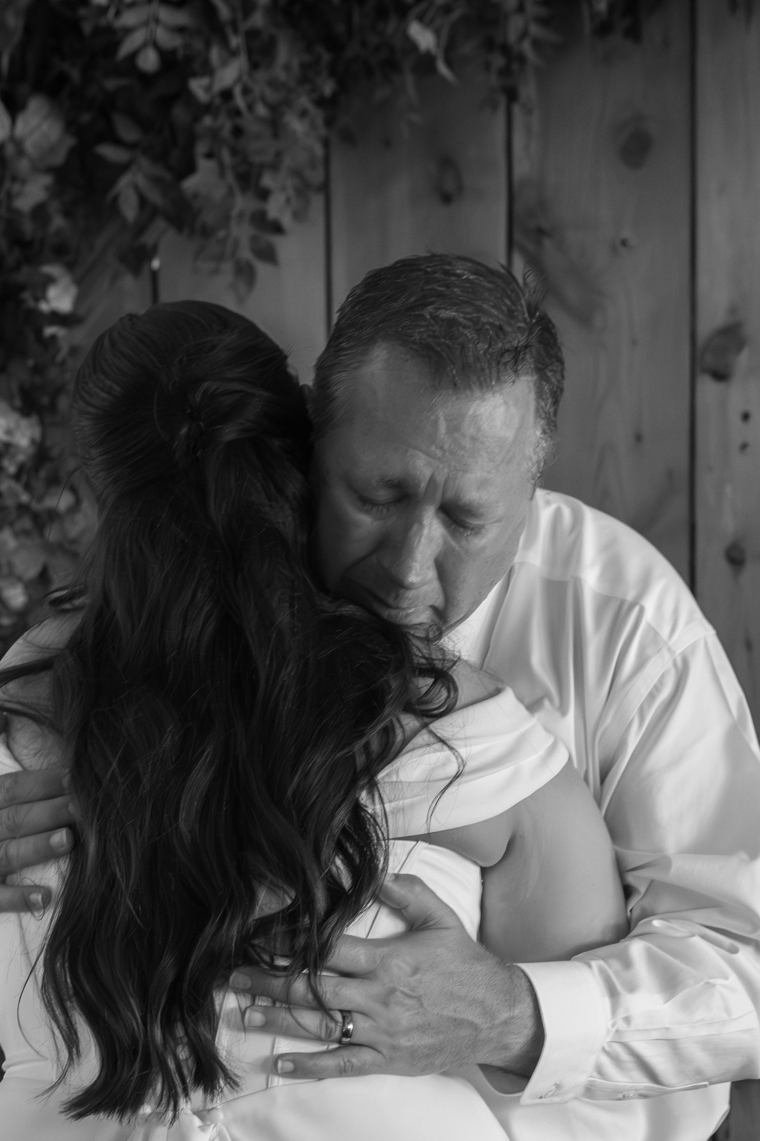 Black and white photo of a man in white shirt embracing and kissing a woman with long dark hair at a wedding.